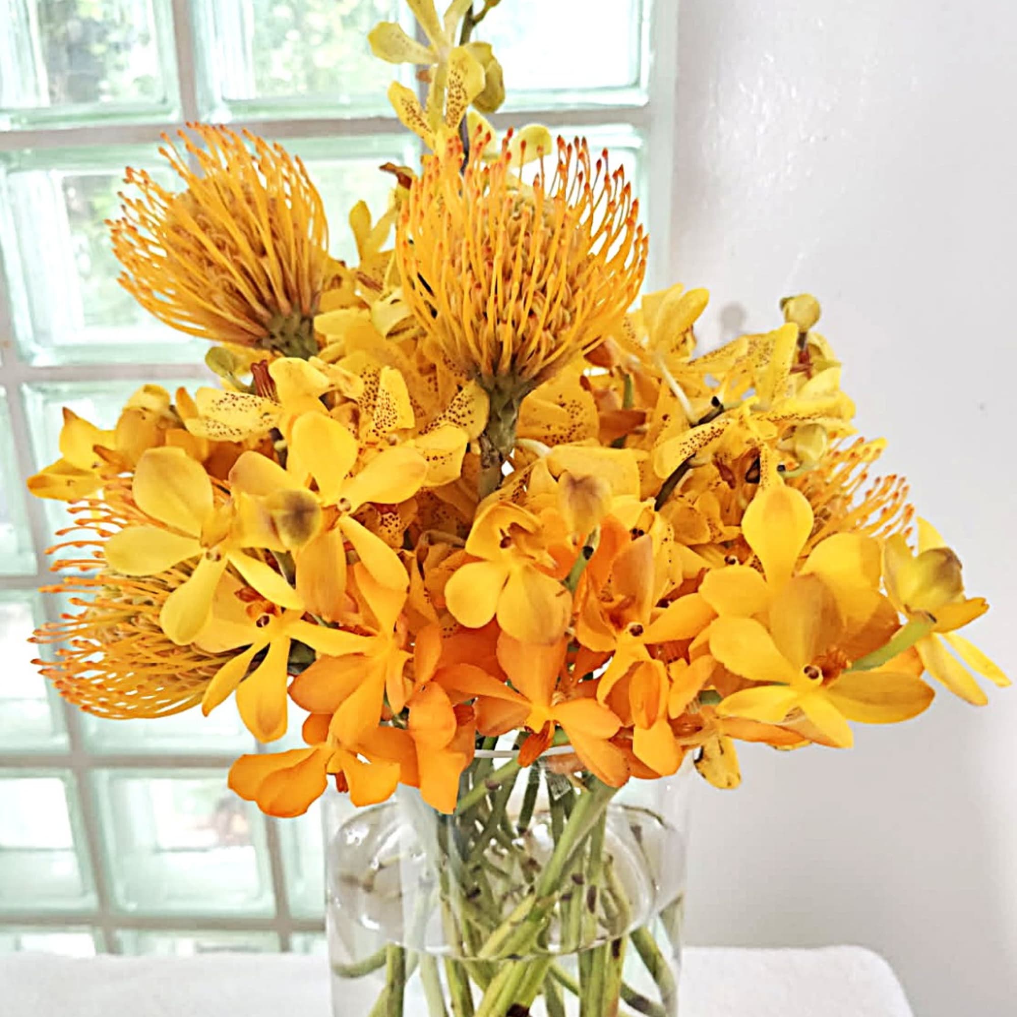 Orange and yellow tropical flowers arranged in a clear glass vase
