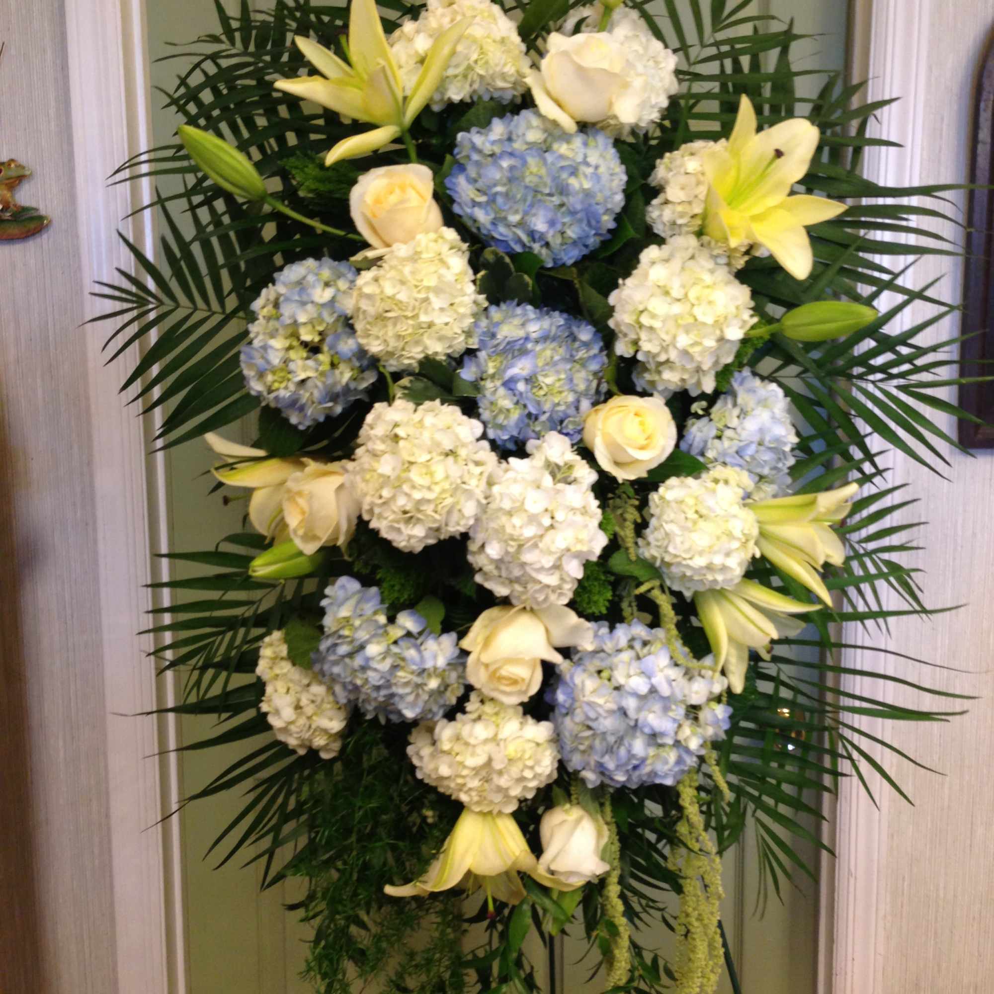 Tall standing floral spray with white lilies, roses, and blue hydrangeas