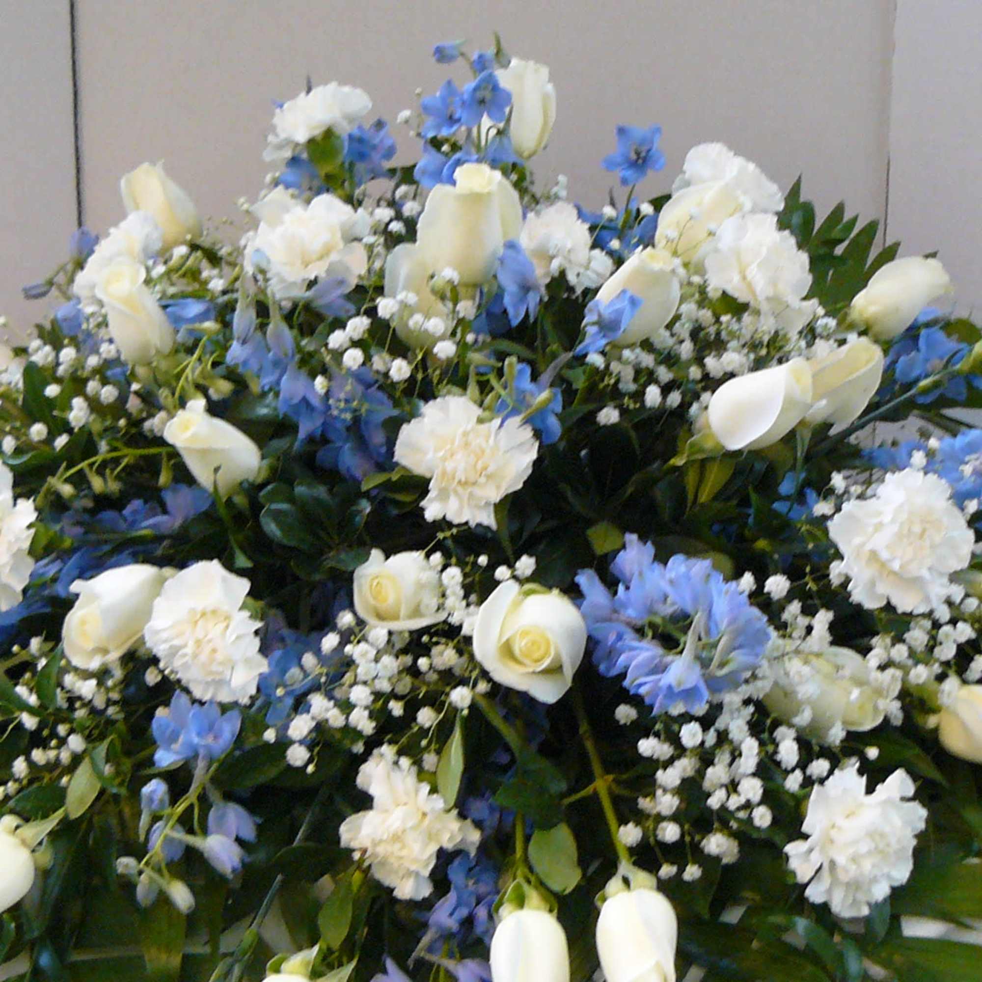A broad, low casket spray in cool white and blue tones designed