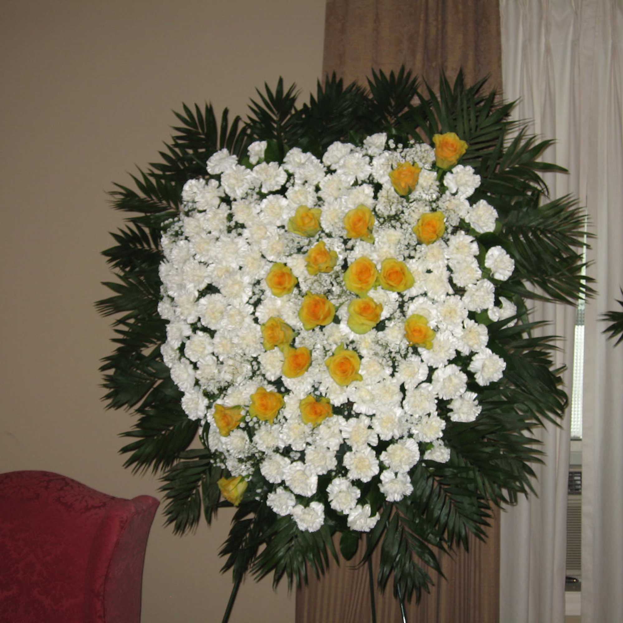 Standing floral spray of white and yellow flowers on a dark green frame