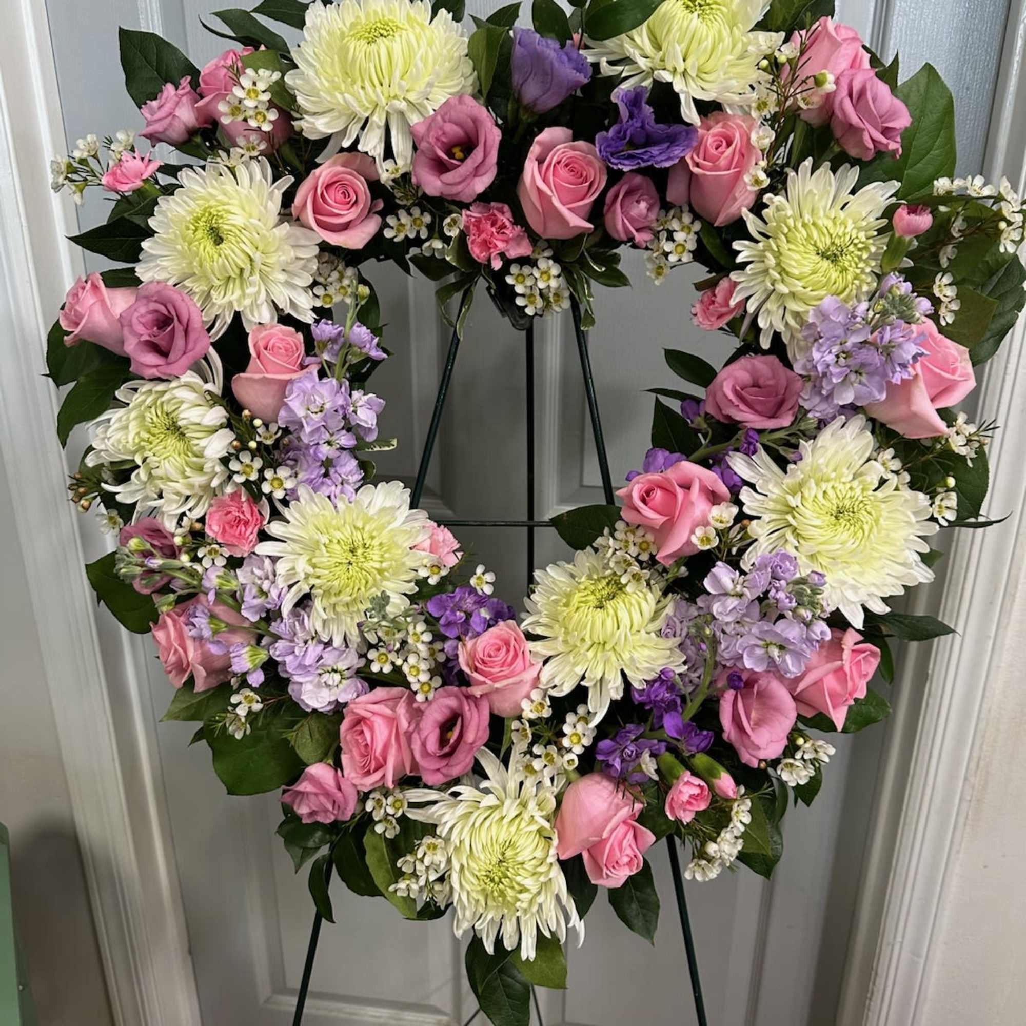 Heart-shaped floral wreath with pink roses and white chrysanthemums on an easel
