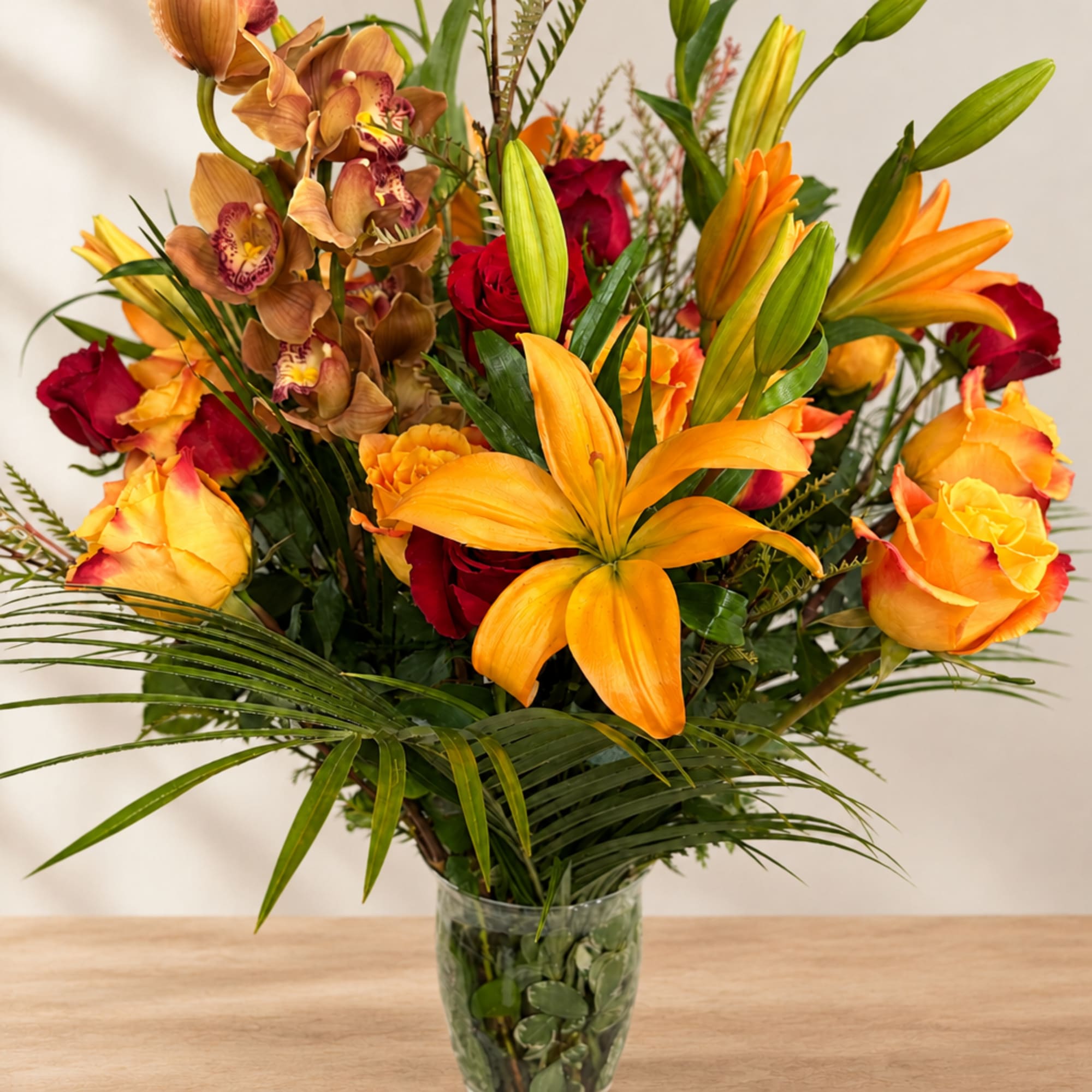 Bouquet of orange lilies, red roses, and orchids in a glass vase