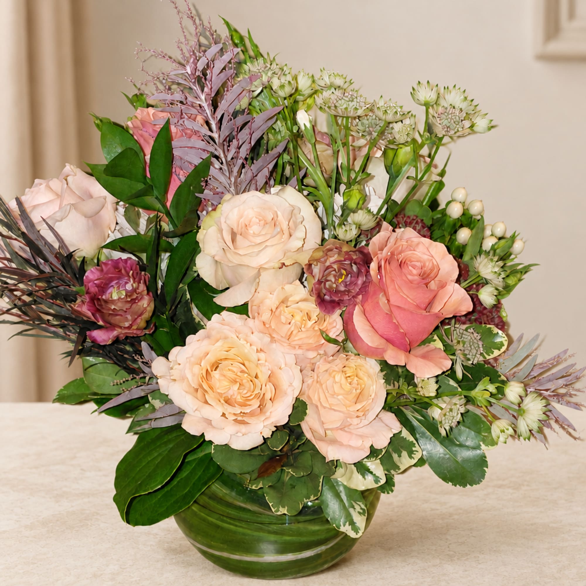 Mixed pink and peach roses in a green glass vase
