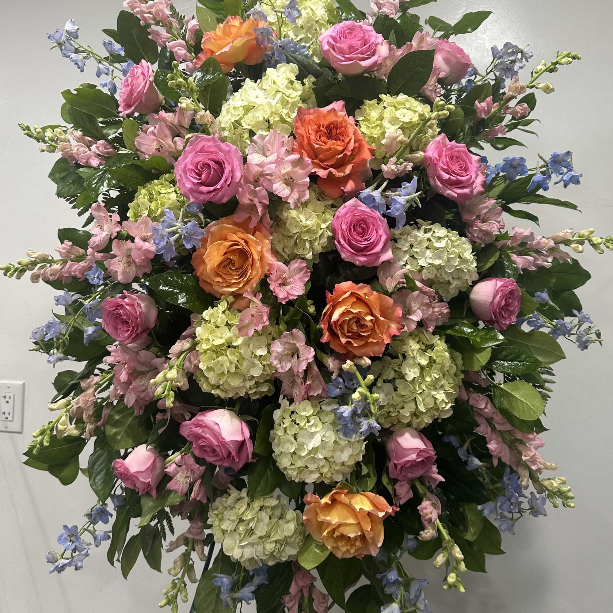 Large standing floral spray with pink and orange roses, hydrangeas, and blue delphinium