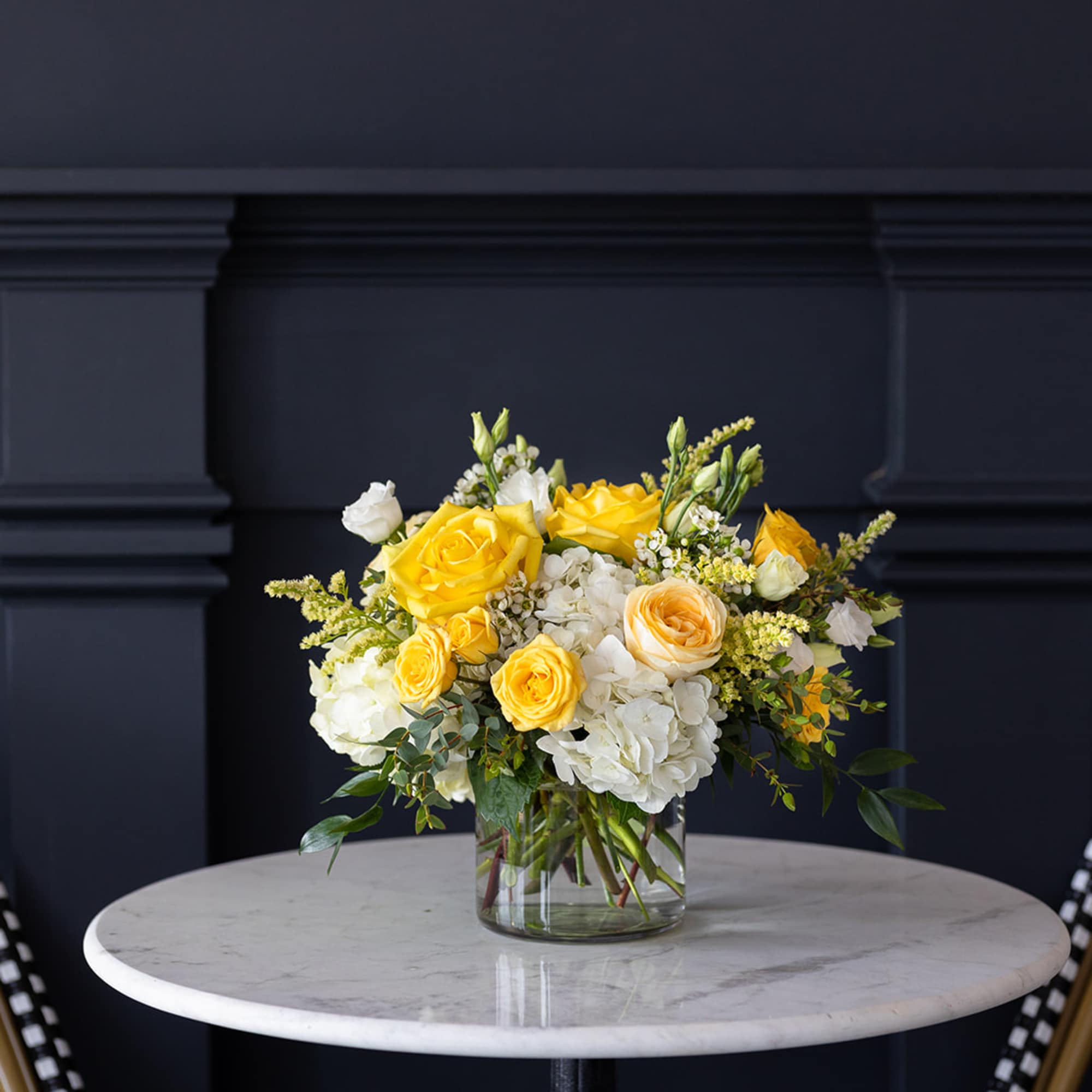 Yellow and white roses arranged in a clear glass vase on a table