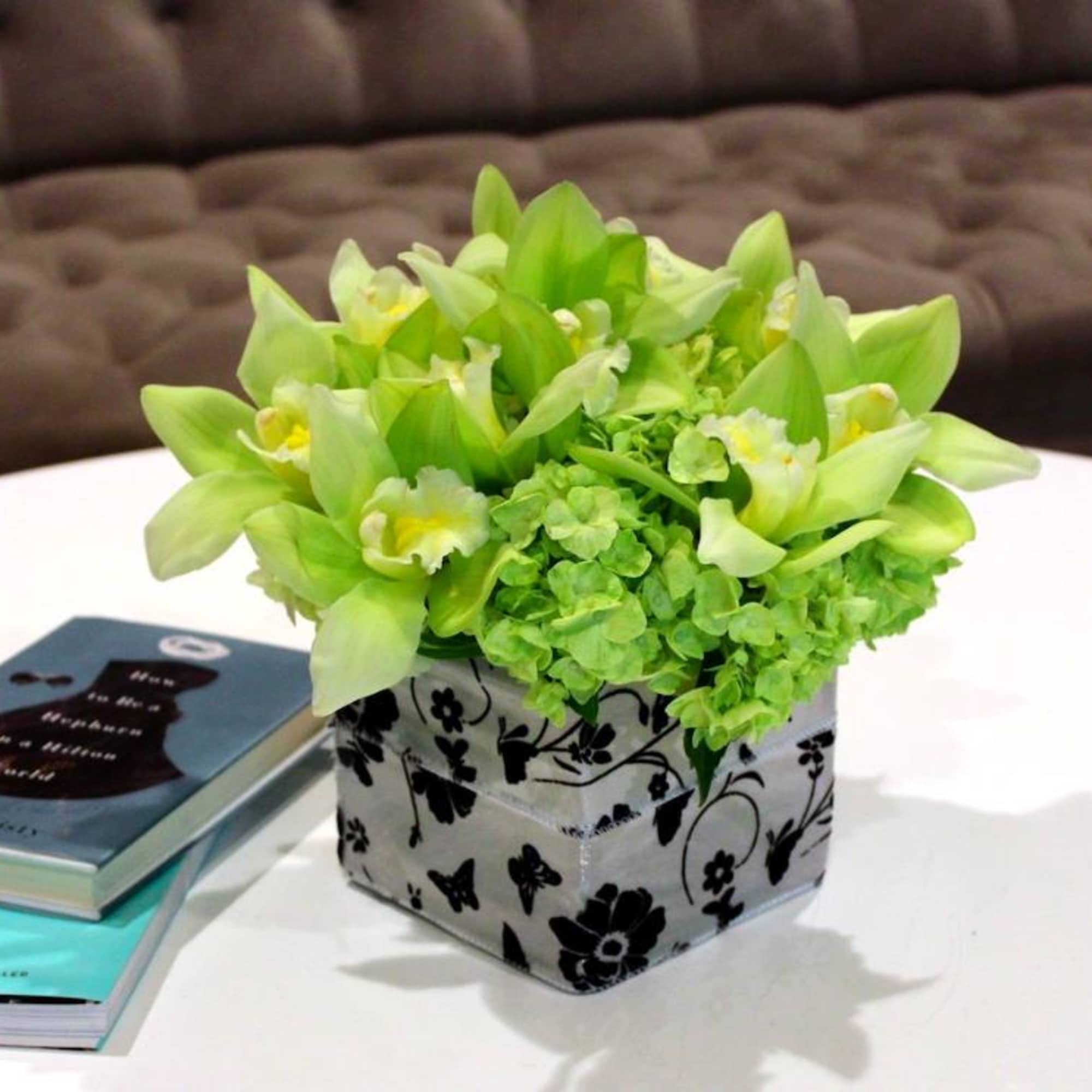 Green orchid arrangement in a patterned square box on a table