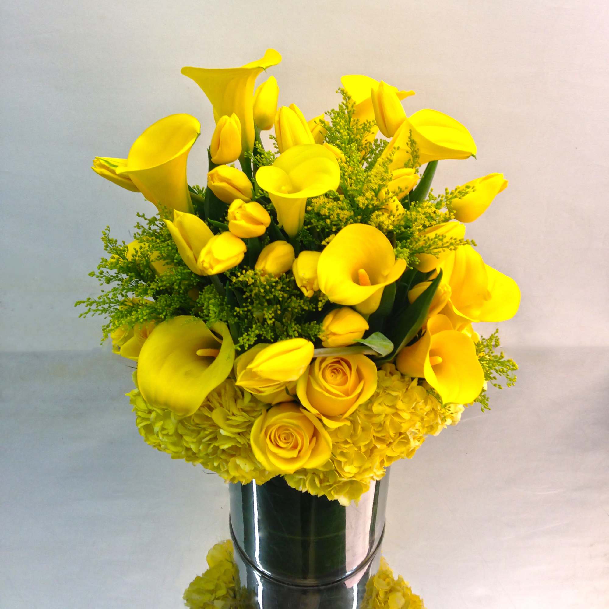 Yellow calla lilies and roses arranged in a glass vase
