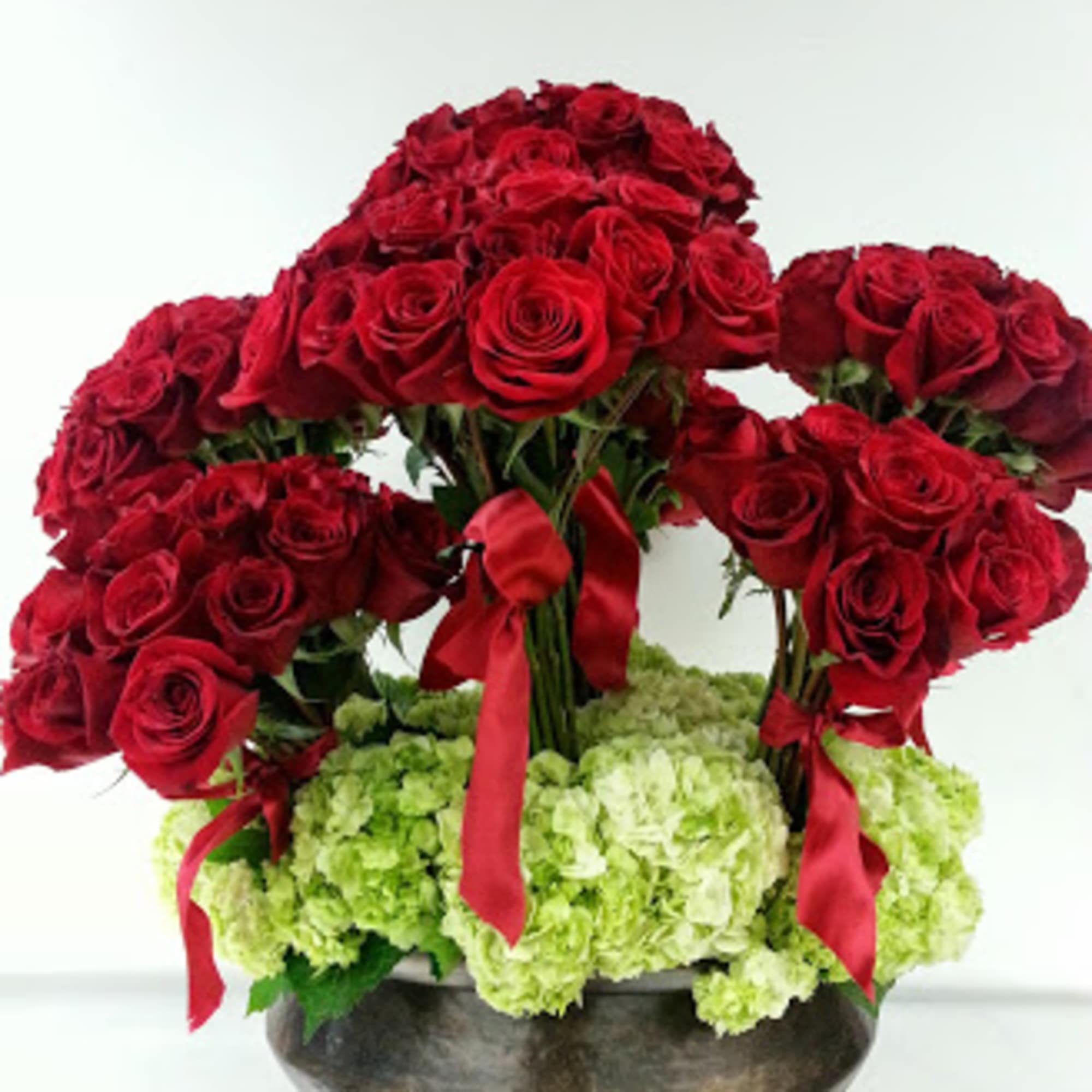 Red rose arrangement with green hydrangeas in a dark bowl vase
