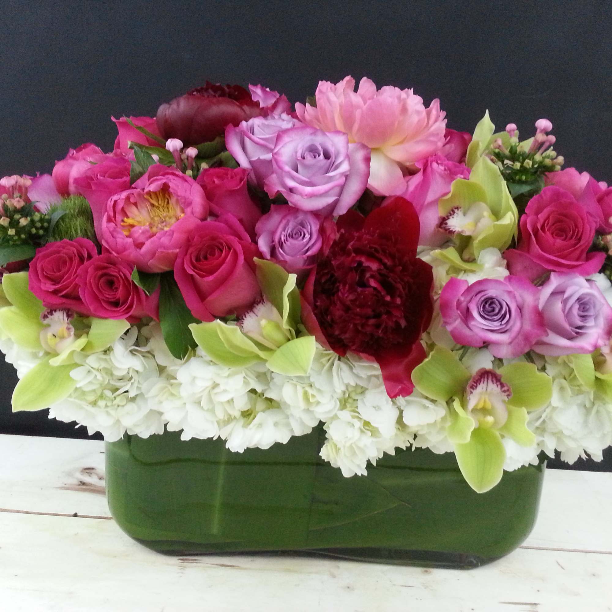 Mixed pink and lavender flower arrangement in a green container