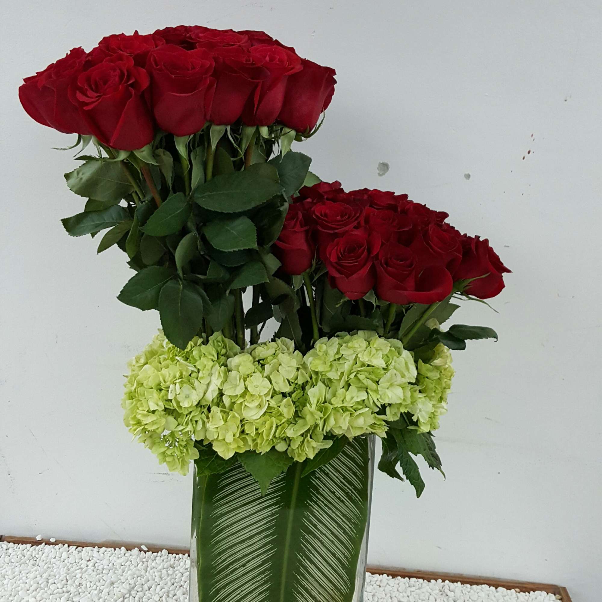 Two red rose arrangements in a glass vase with pale green hydrangeas and a candle