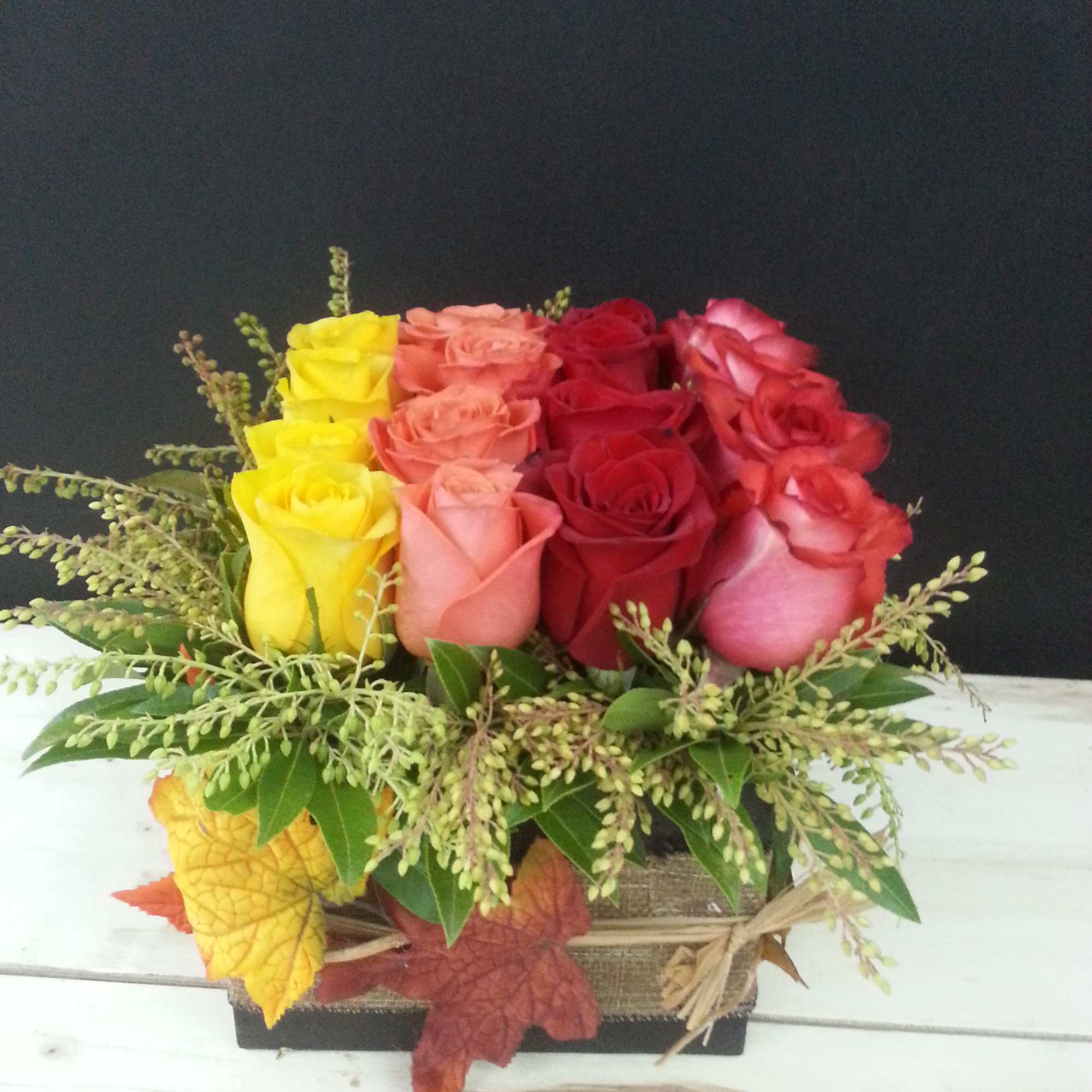 Colorful rose arrangement in a rectangular basket with autumn leaves