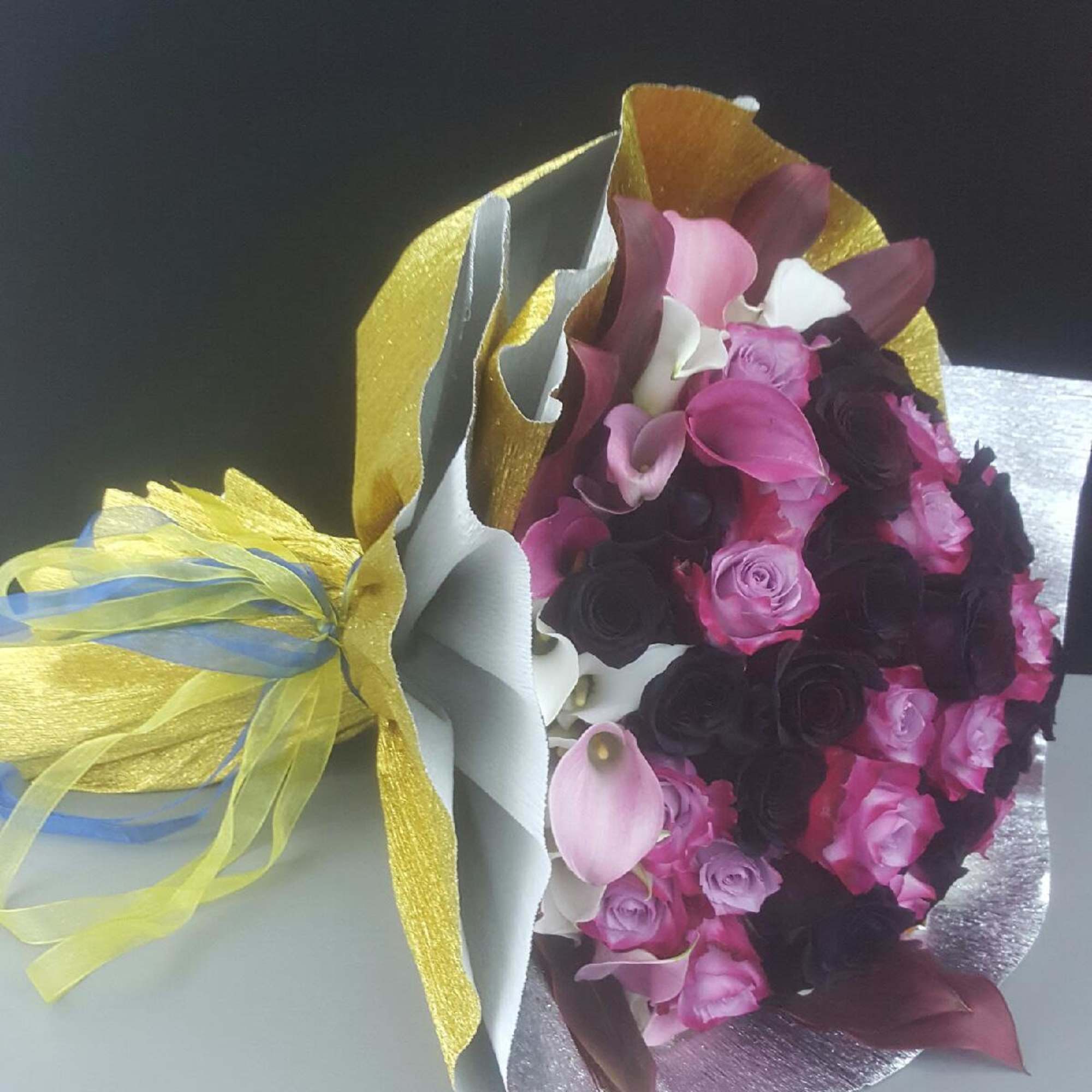 Bouquet of pink, white, and dark roses with calla lilies wrapped in metallic paper
