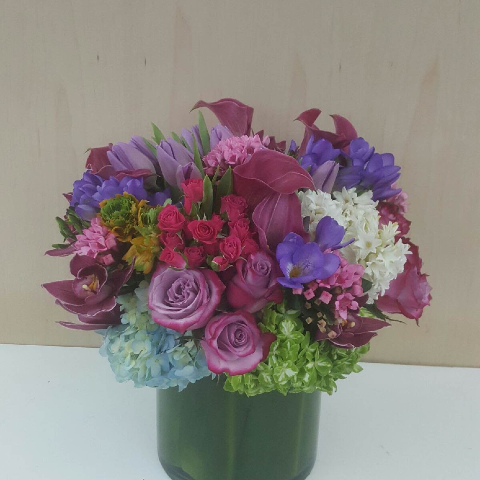 Mixed bouquet of purple, pink, white, and blue flowers in a green vase