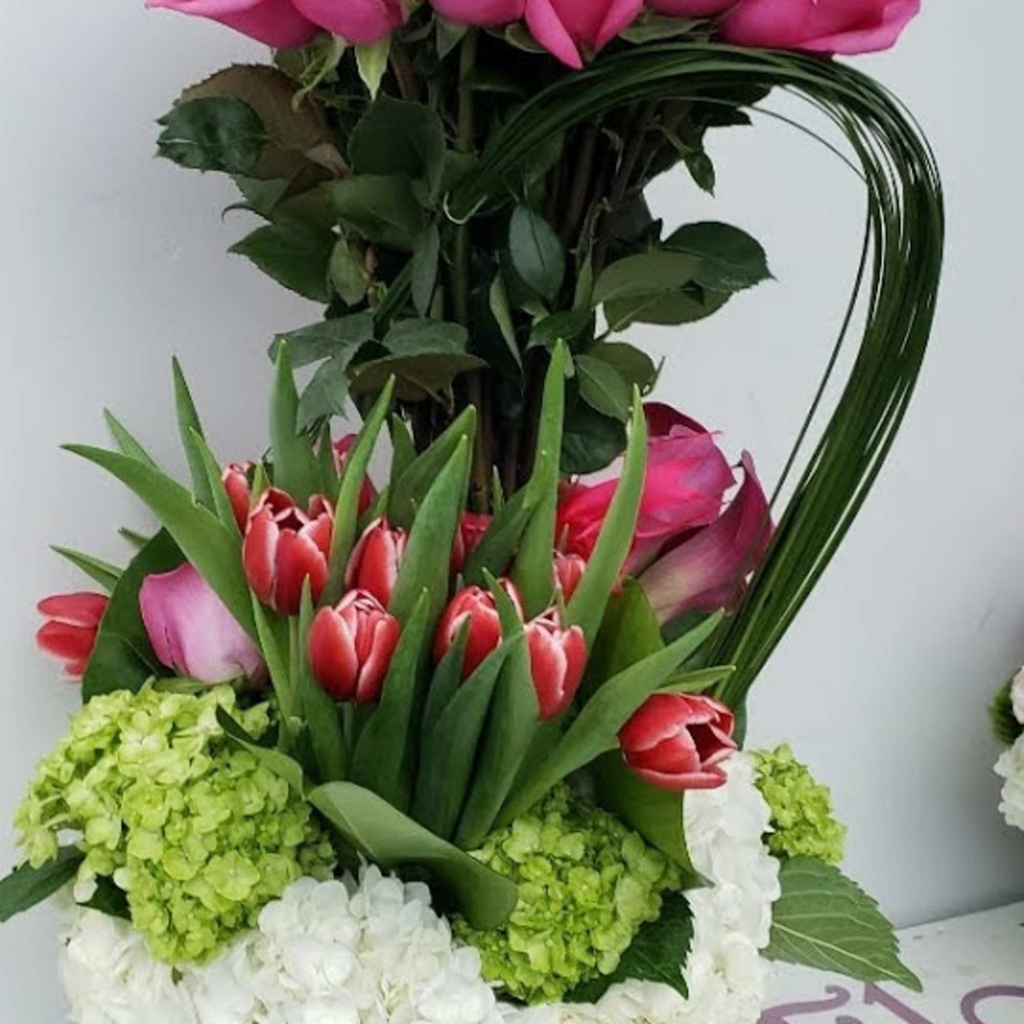 Pink roses and tulips arranged in a glass vase with hydrangeas