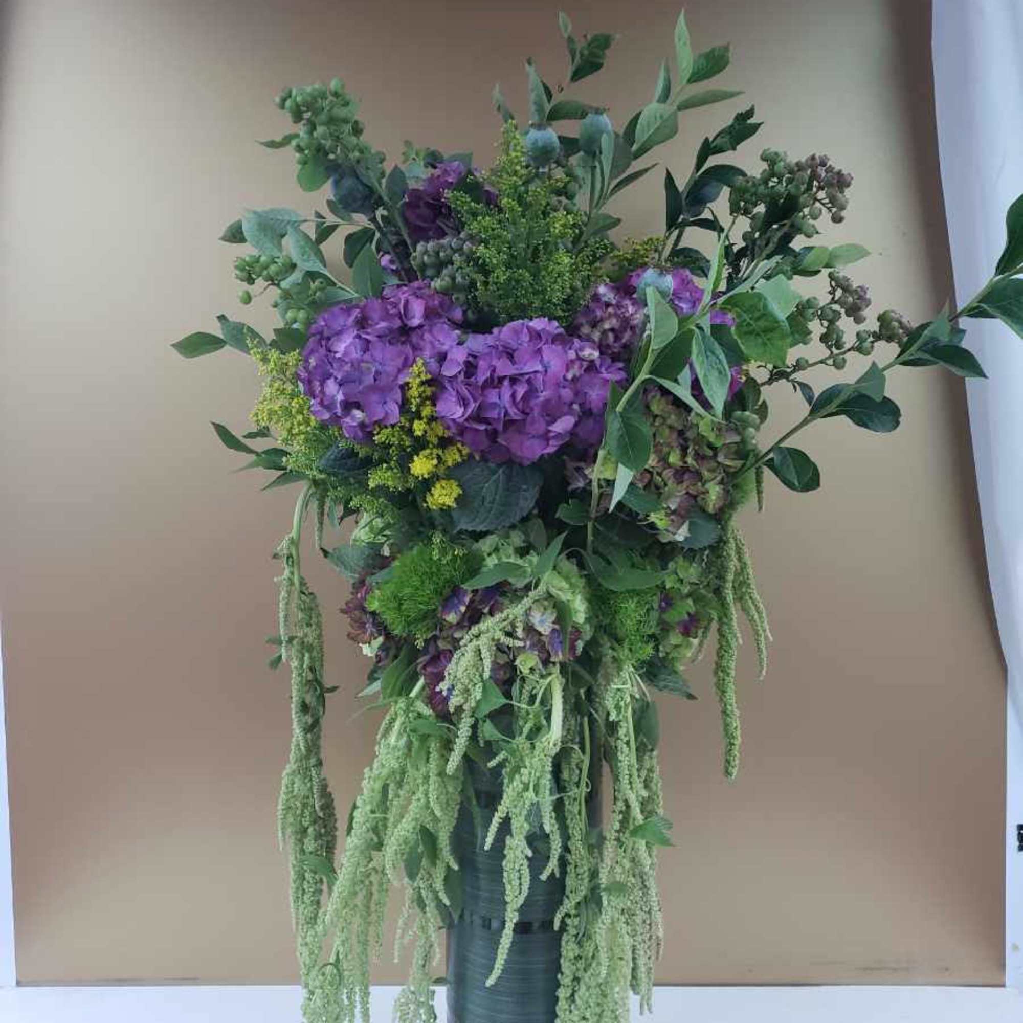 Tall purple floral arrangement in a dark vase with trailing greenery