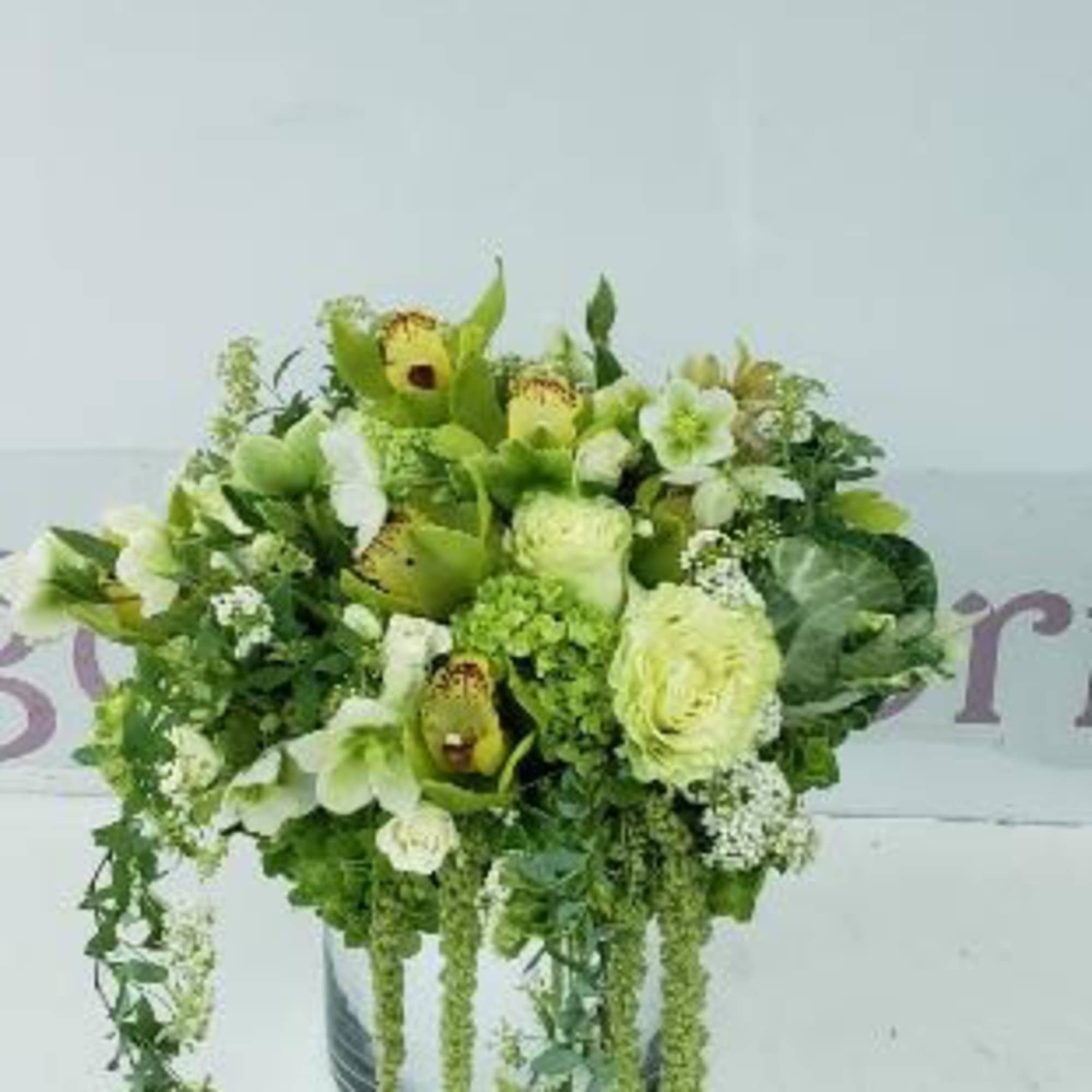 Green and white floral arrangement in a round container