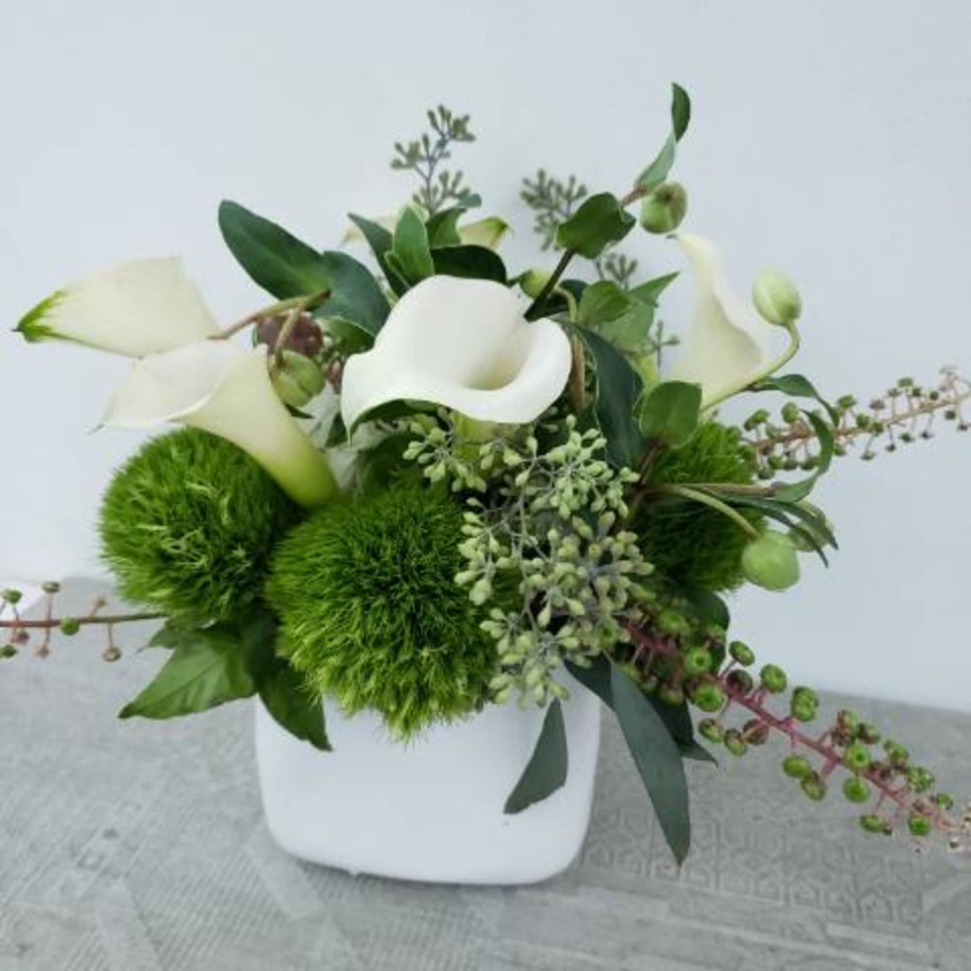 White calla lilies and green pom-pom flowers in a white vase