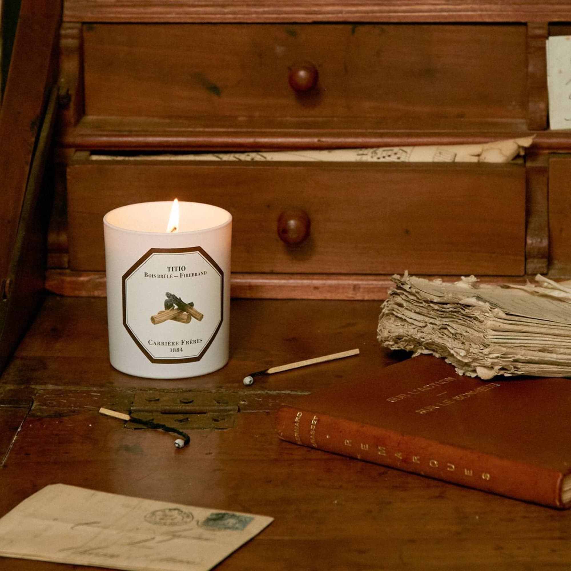 Lit candle on a wooden desk with matches and books
