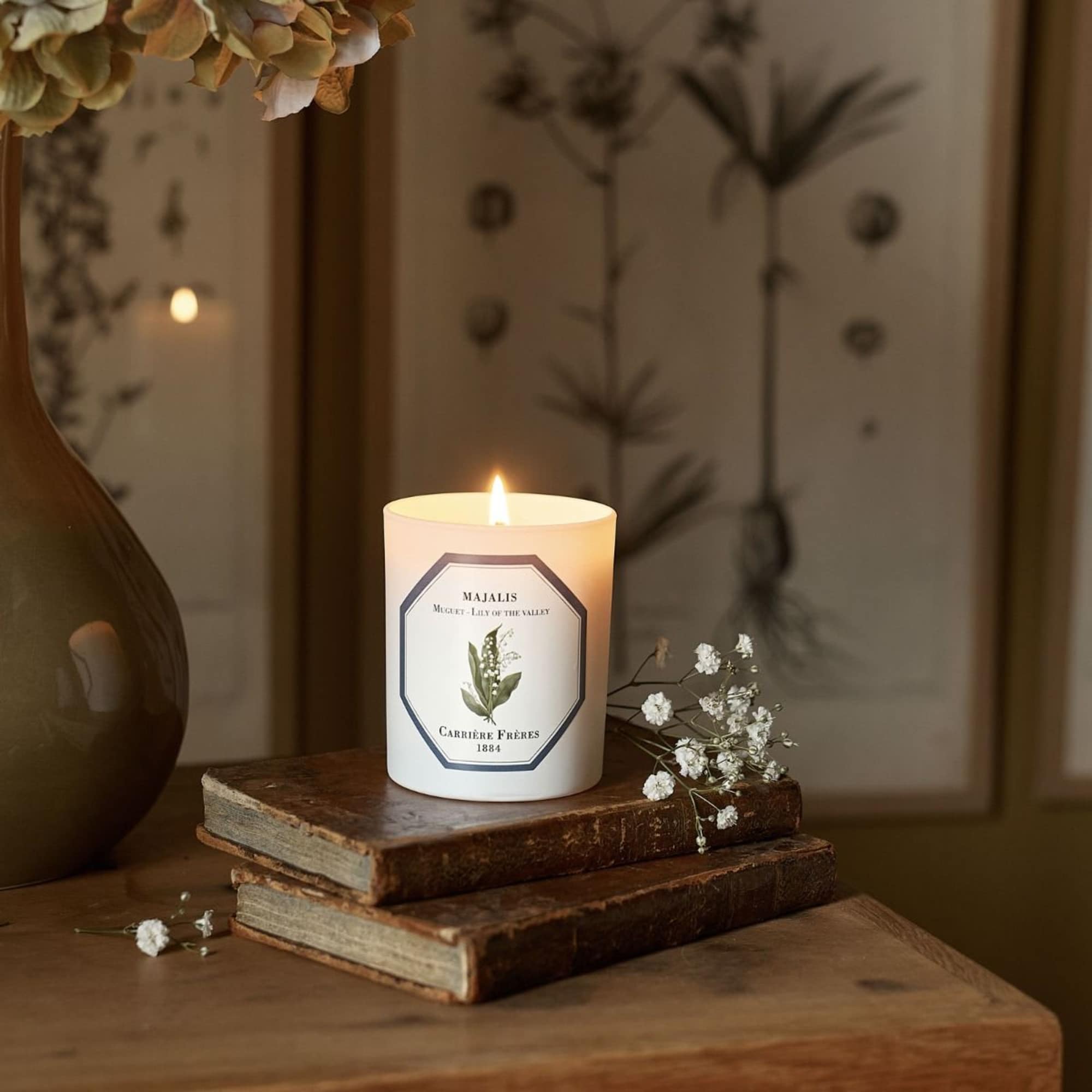 Lit candle on stacked books with small white flowers nearby