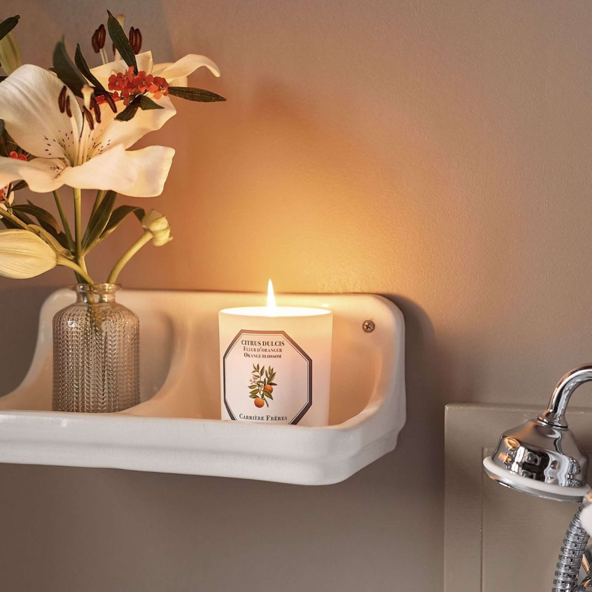 White lilies in a glass vase beside a lit candle