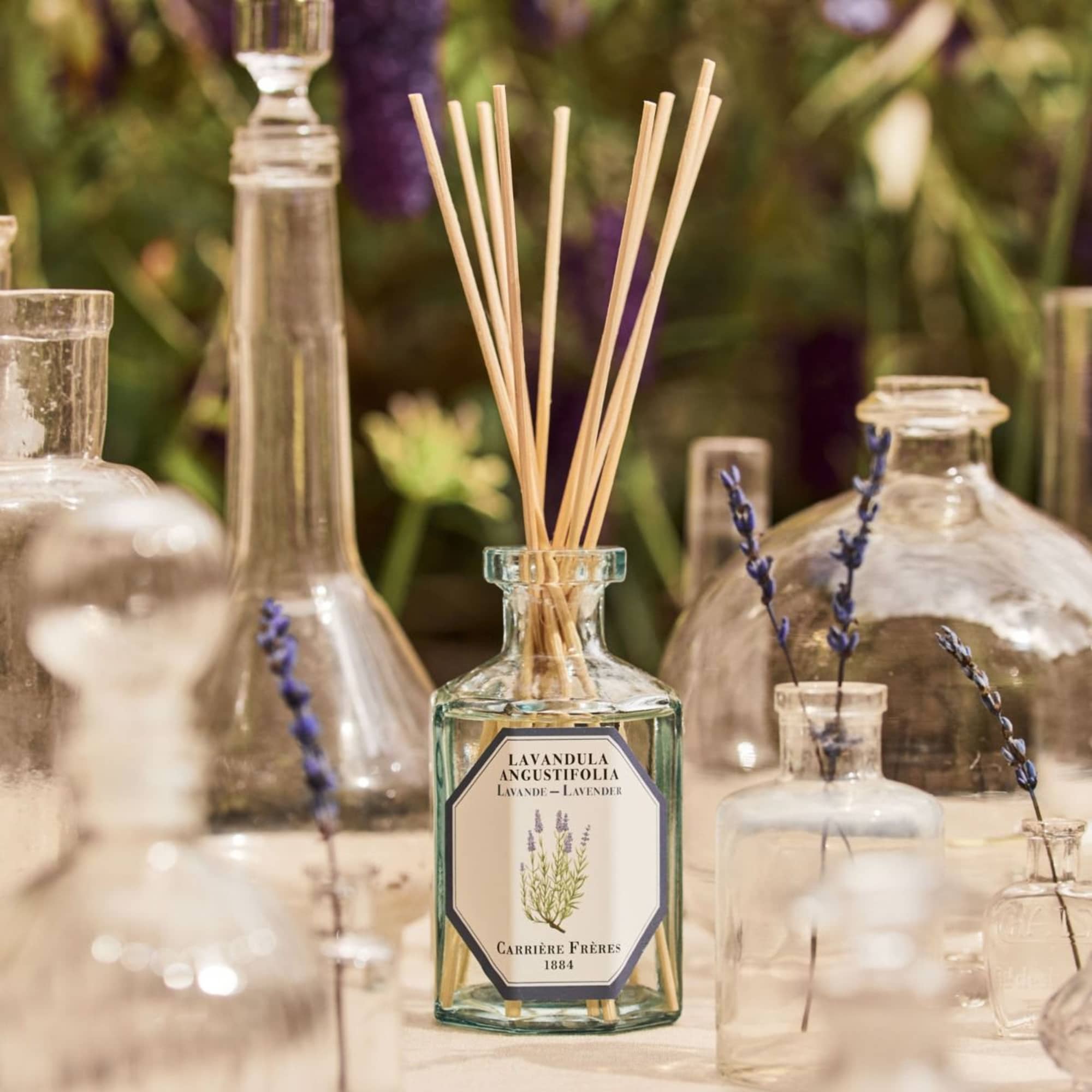 Glass bottles with lavender stems and a reed diffuser bottle on a table
