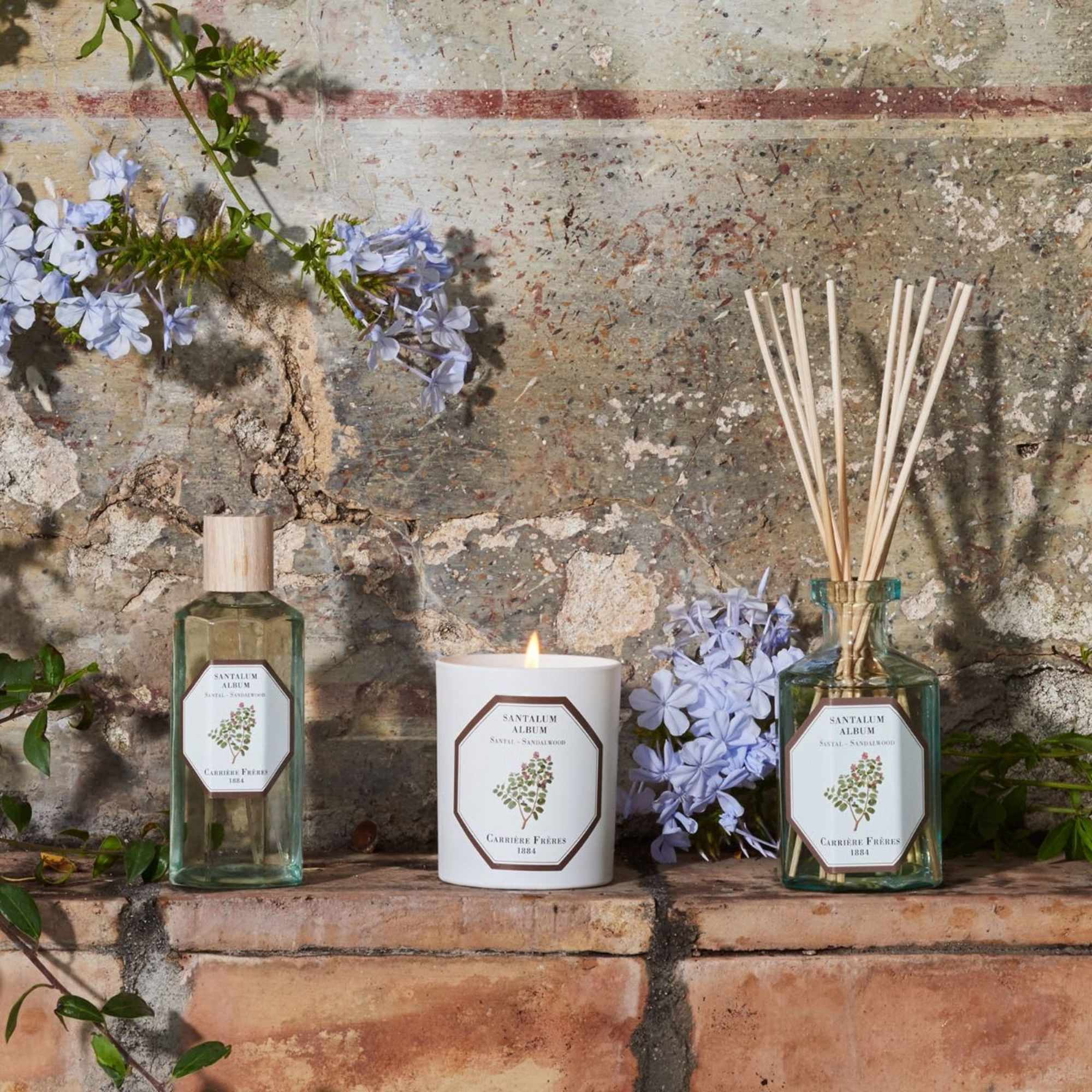 Lavender flowers arranged with two reed diffusers and a lit candle on a stone ledge.
