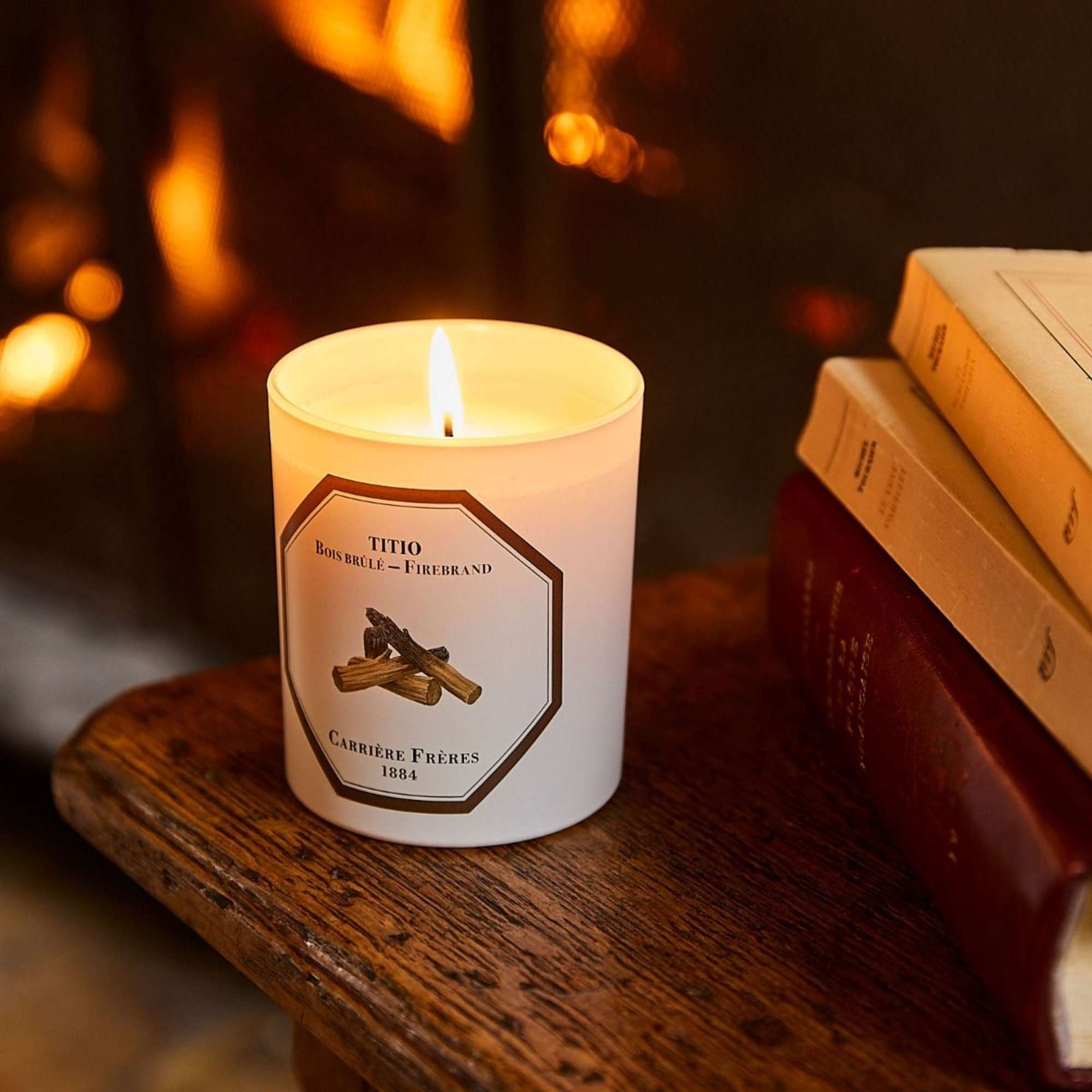 Lit white candle in a glass jar beside stacked books