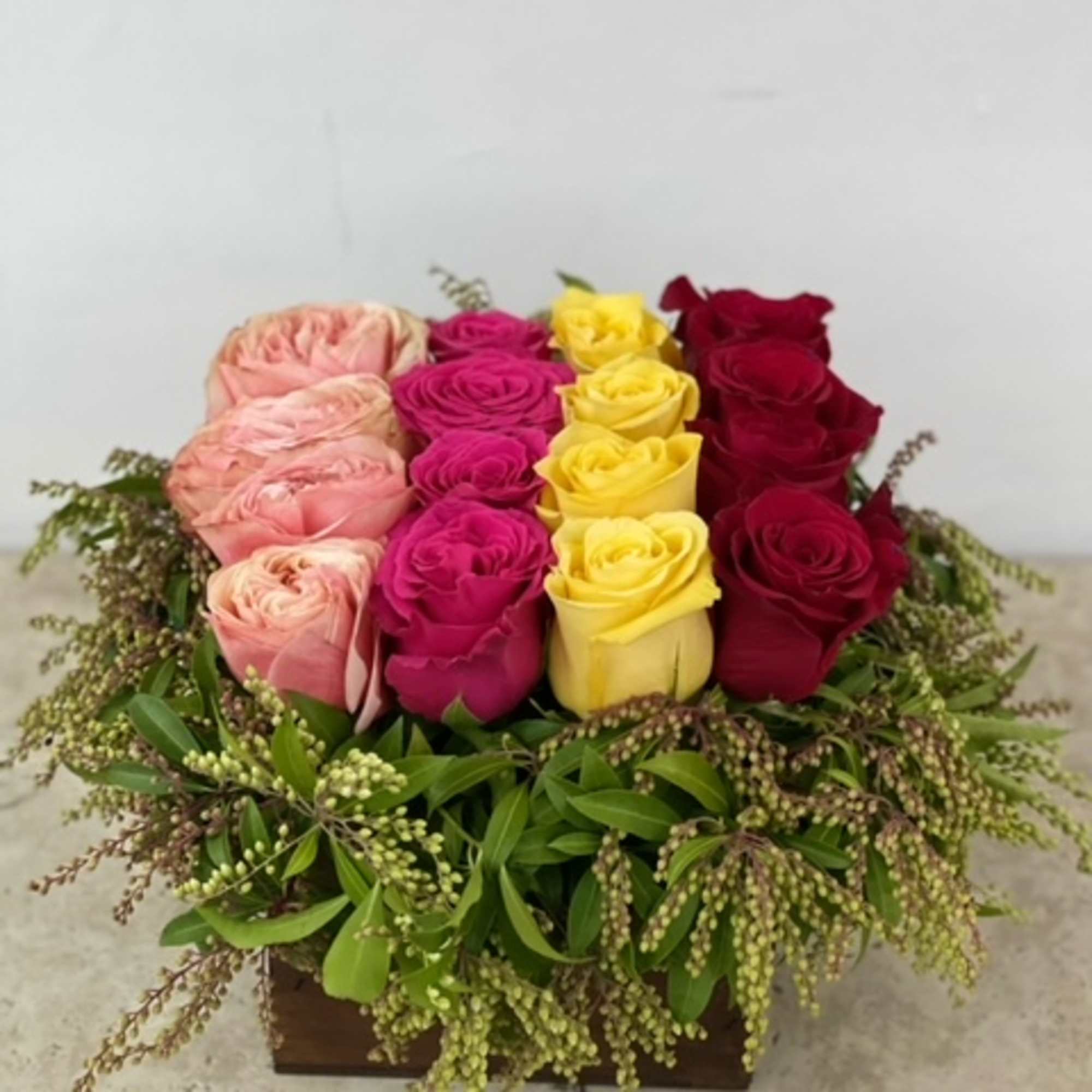 Rectangular arrangement of pink, yellow, and red roses in a low wooden box