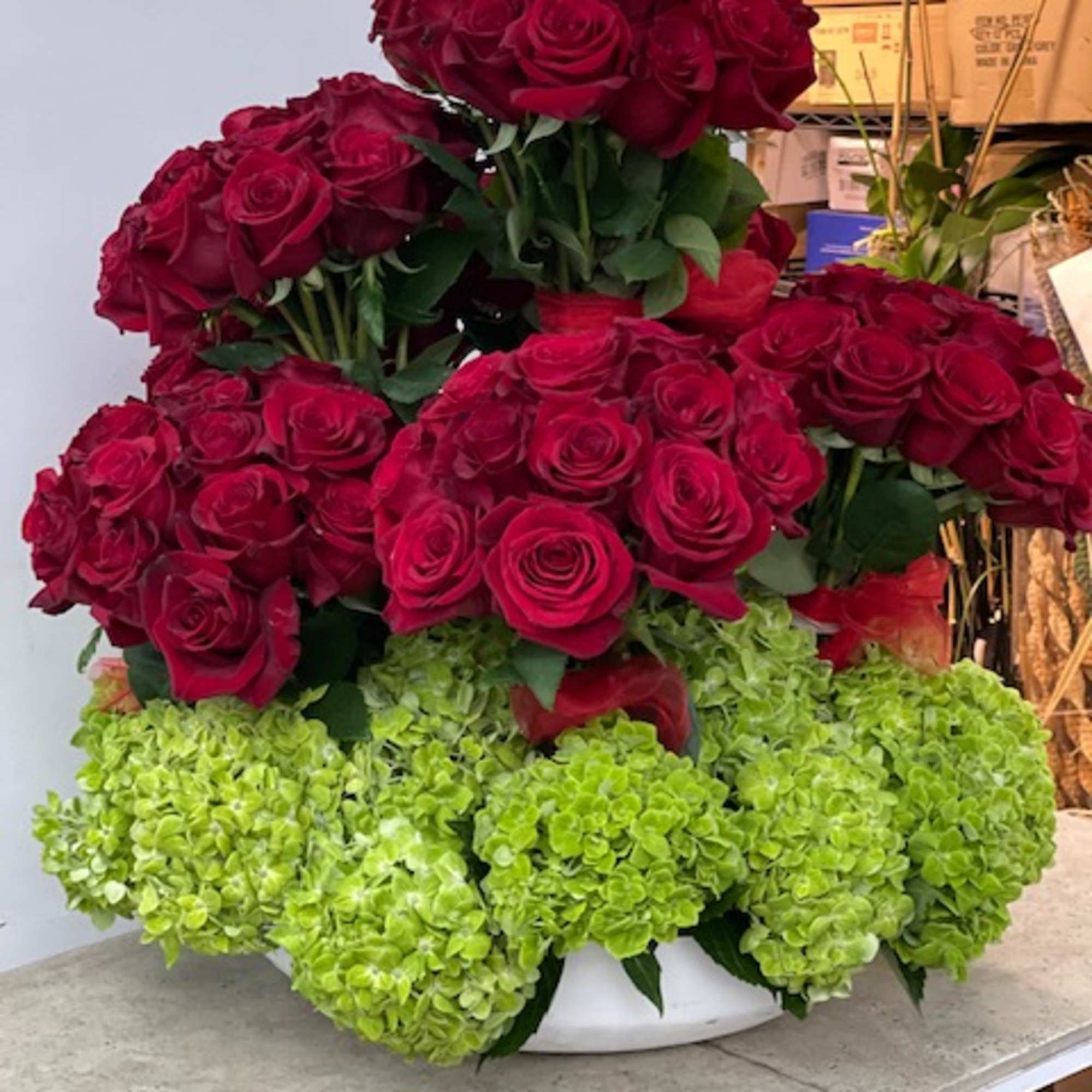 Red rose arrangement with green hydrangeas in a white container