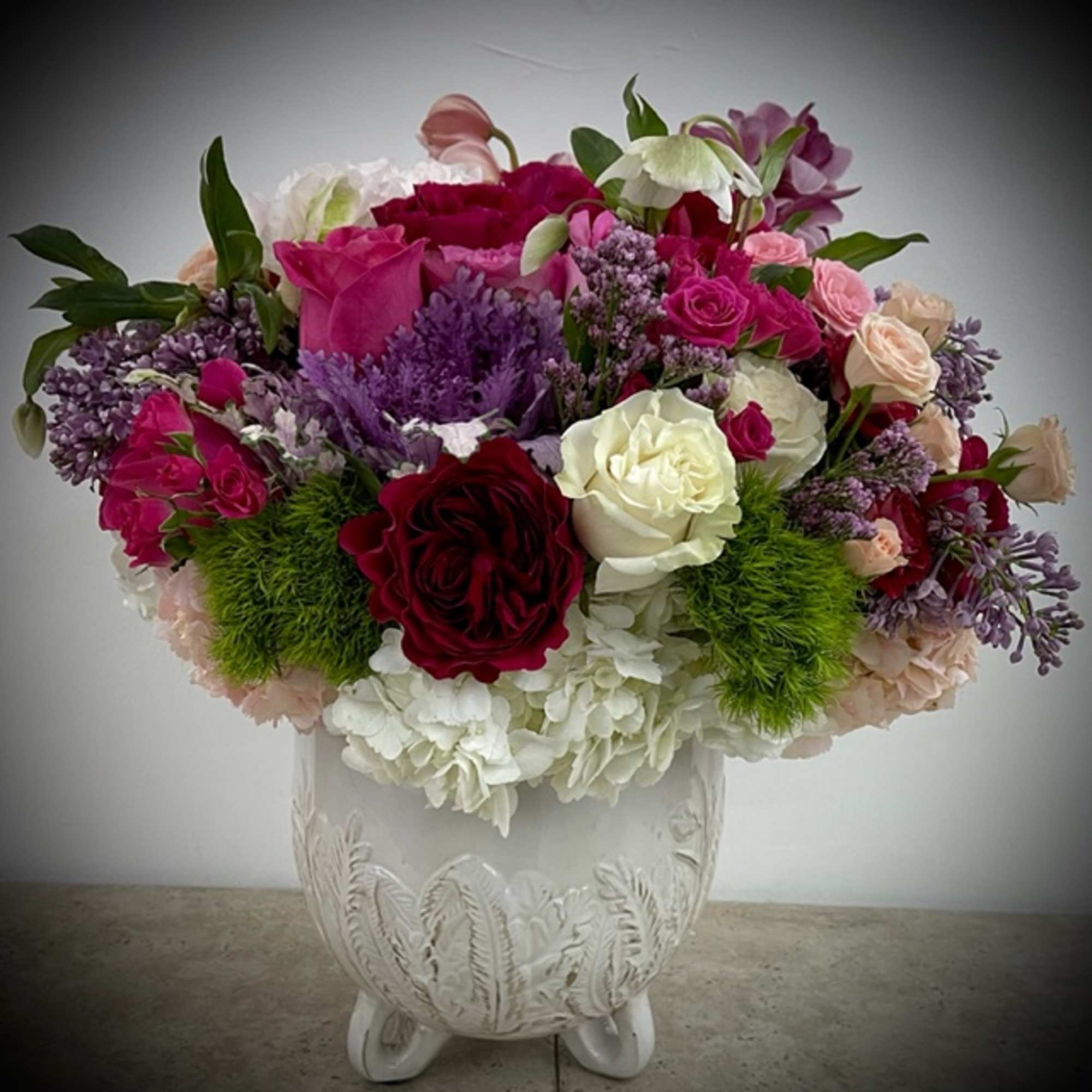 Mixed bouquet of roses, hydrangeas, and purple flowers in a white vase