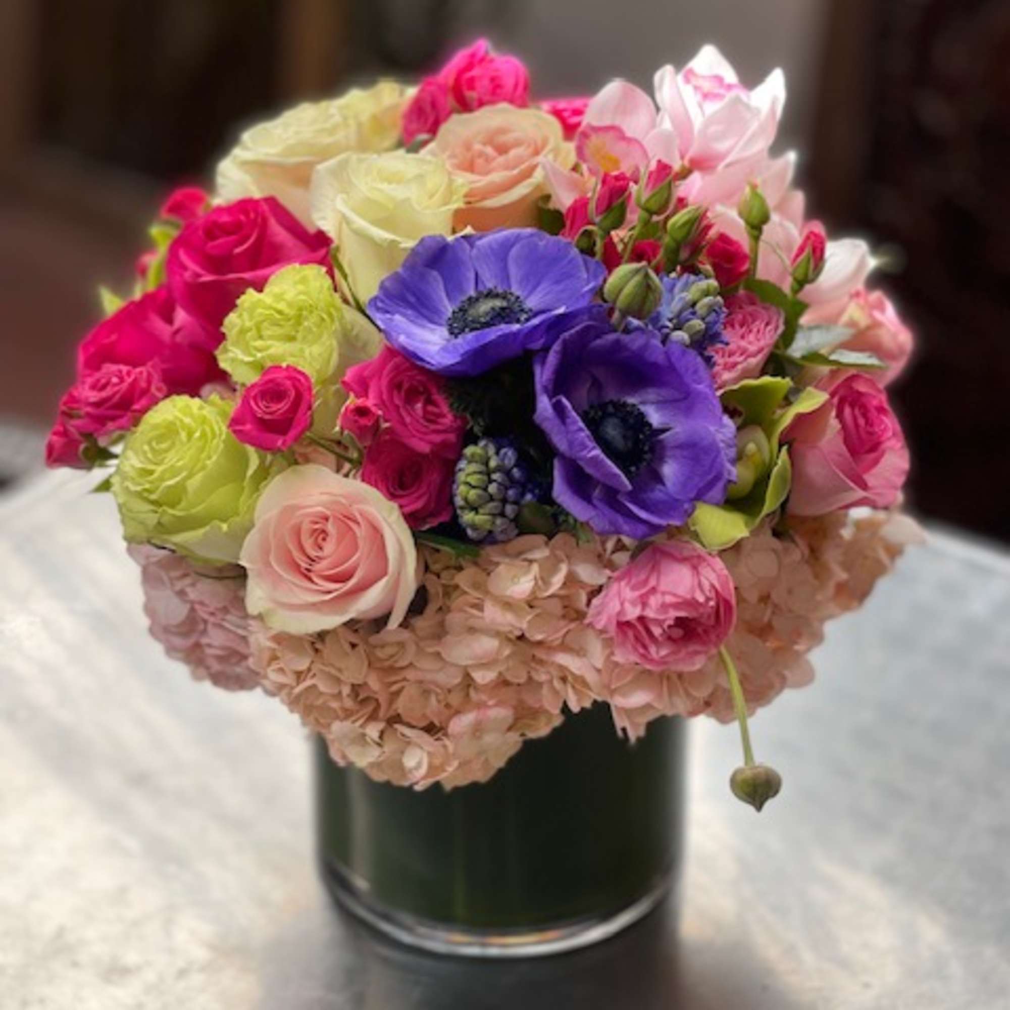 Colorful bouquet of roses, anemones, and hydrangeas in a glass vase