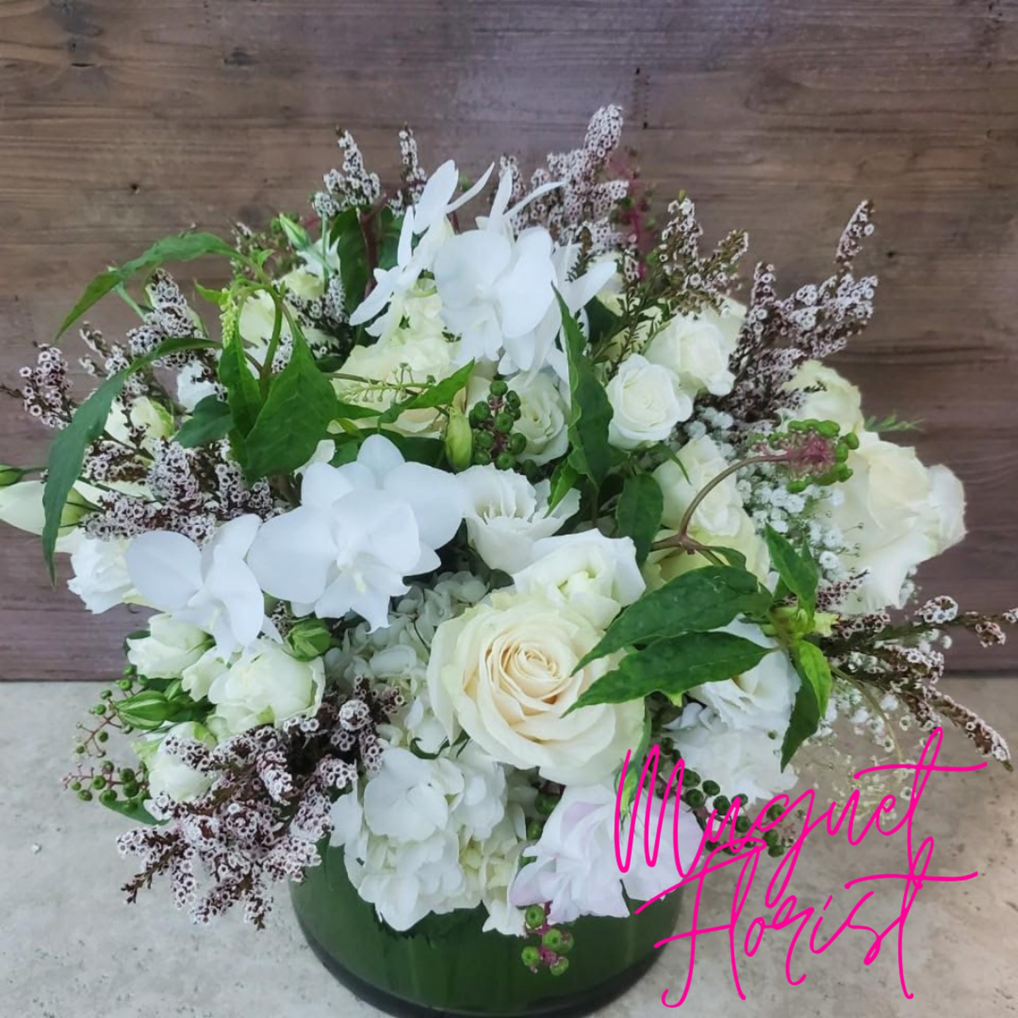 White floral arrangement in a green vase with roses and orchids