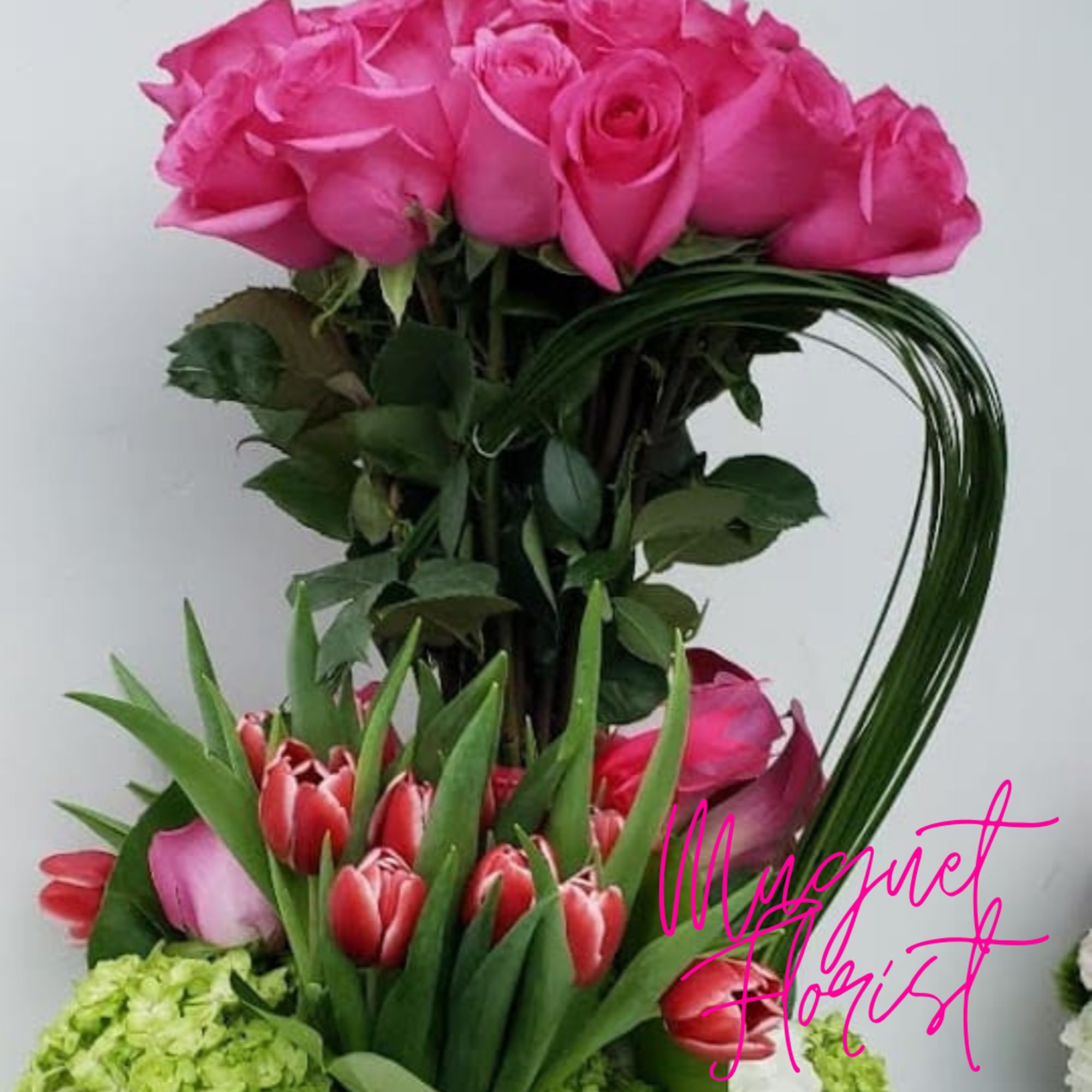 Pink roses above red tulips and green hydrangeas in a tall arrangement