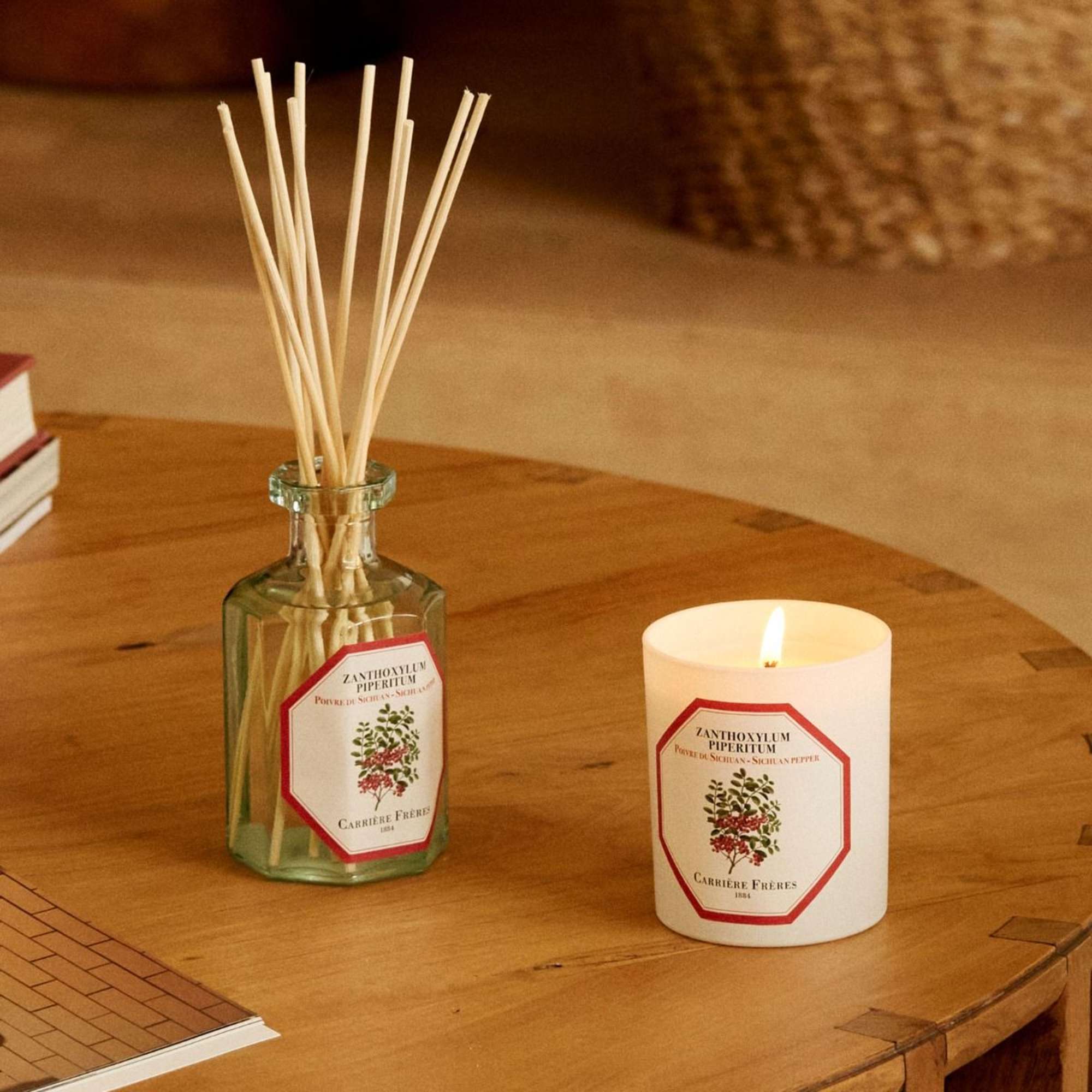 A reed diffuser and lit candle sit on a wooden table.