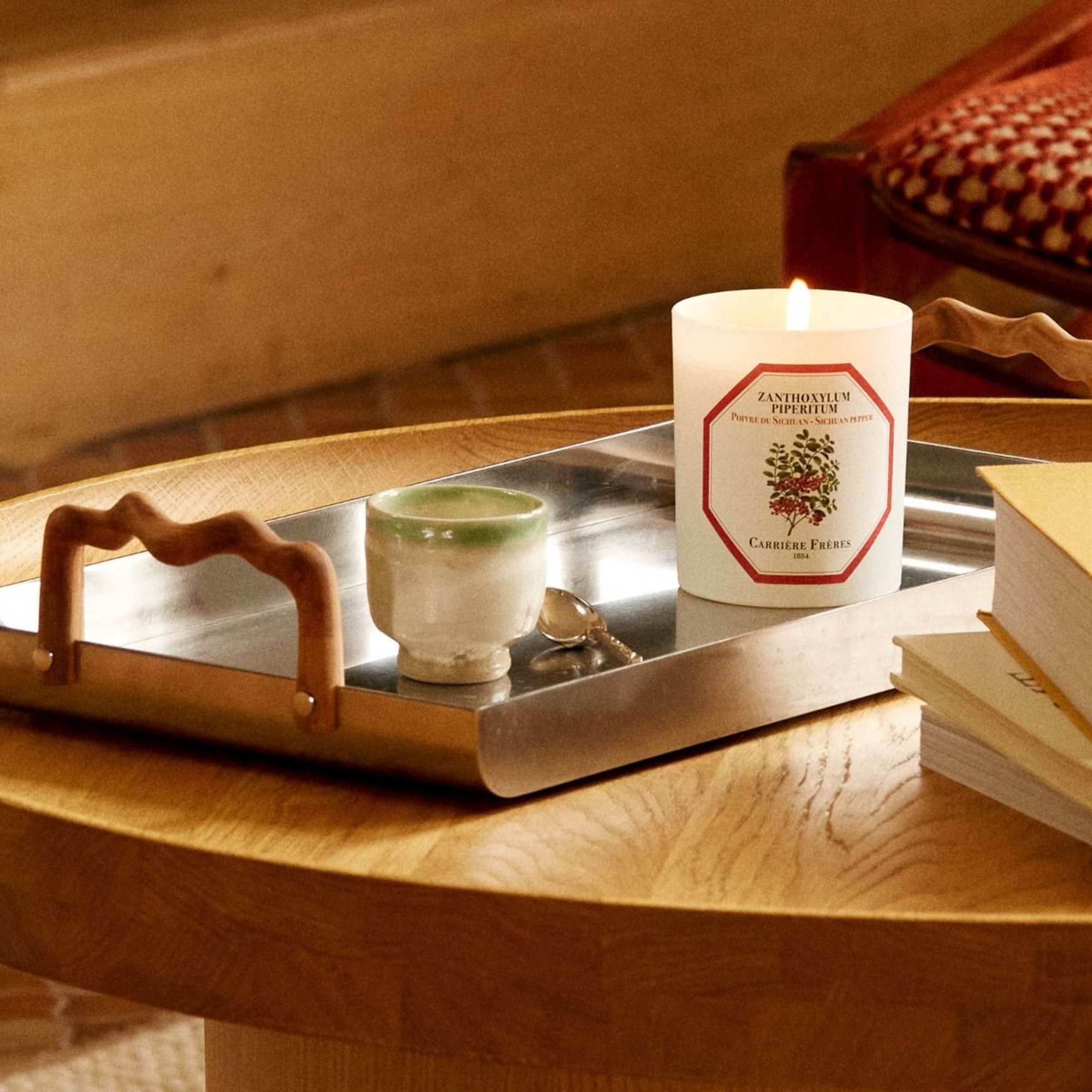 Lit candle on a tray beside a small cup and spoon
