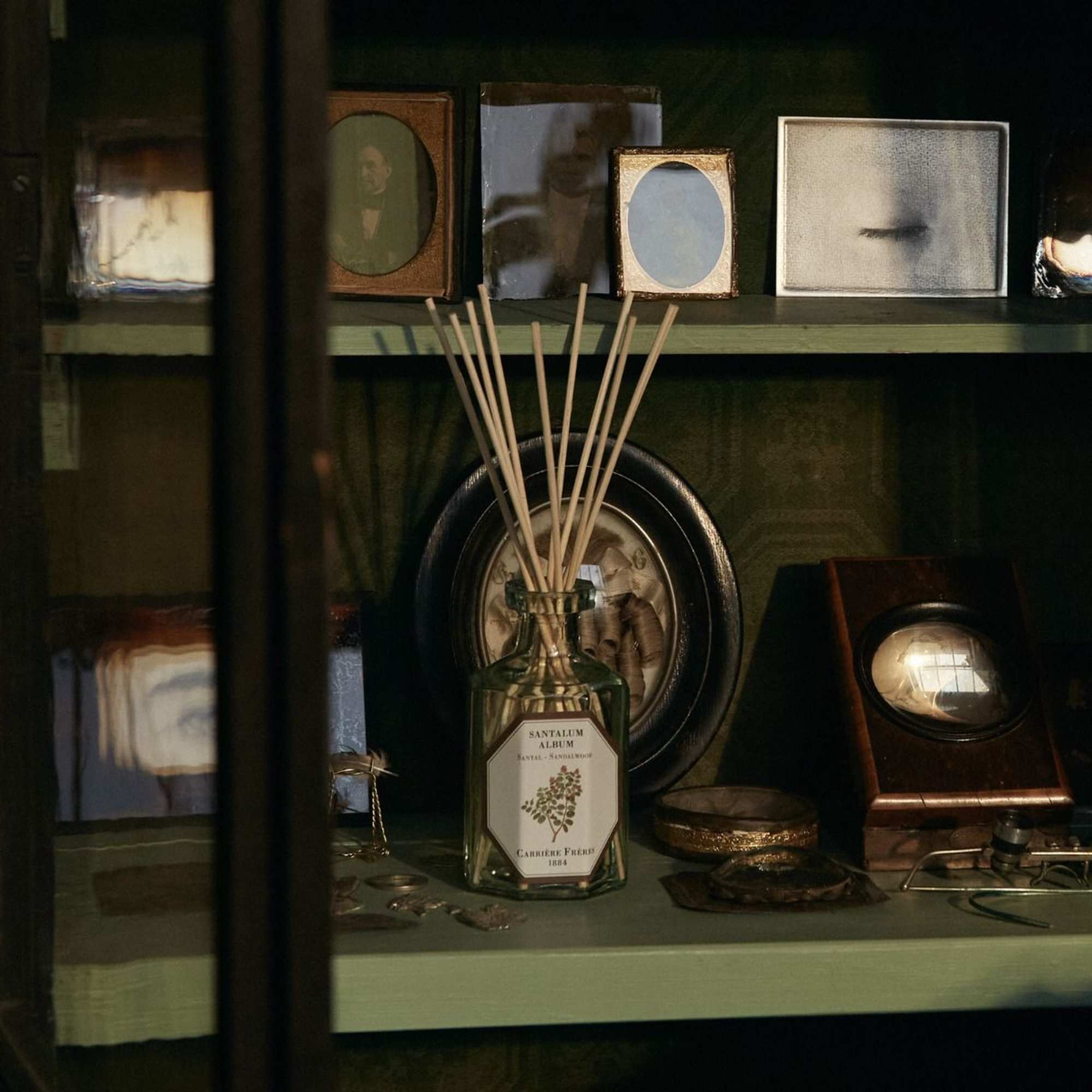 Glass reed diffuser bottle on a shelf with framed objects around it
