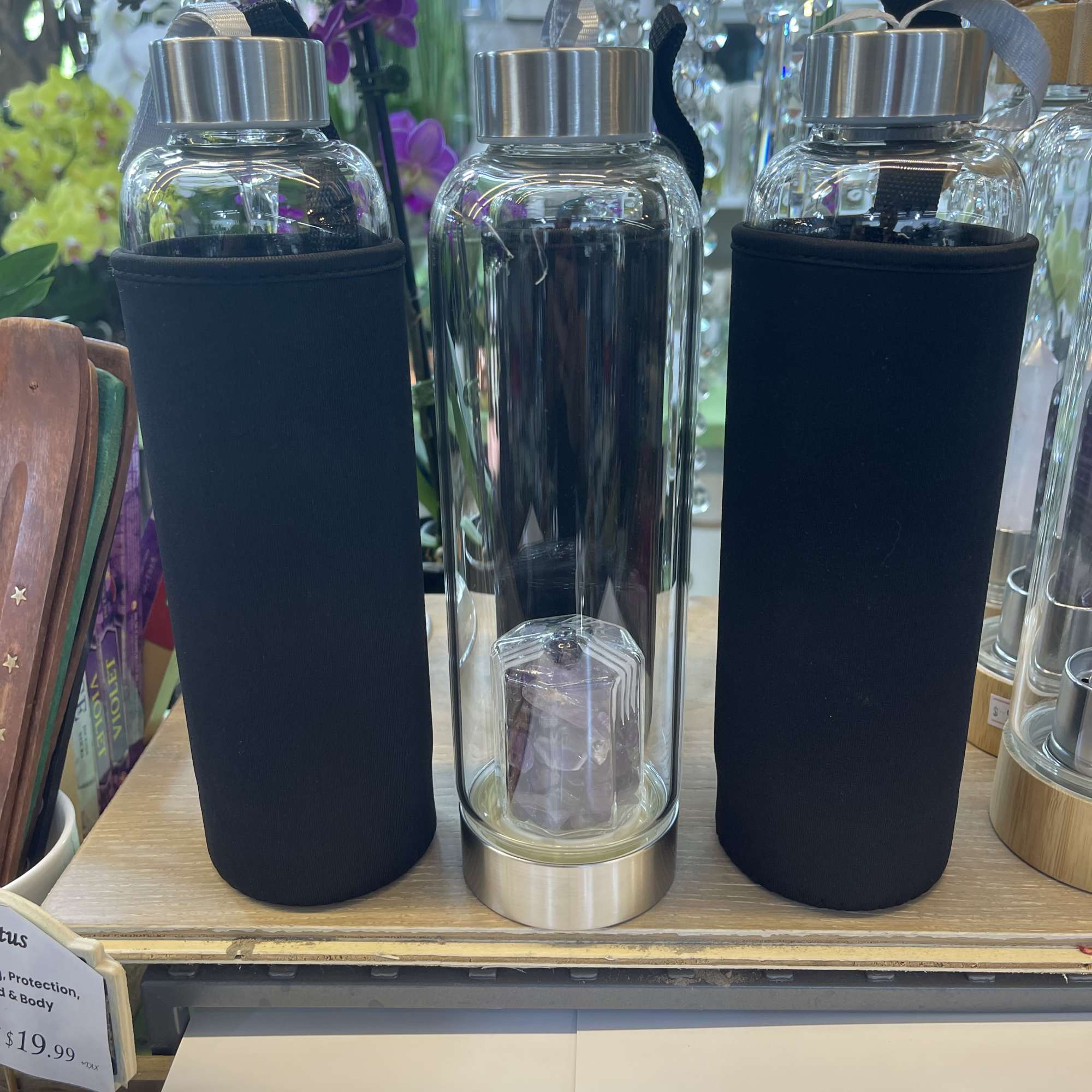 Three clear water bottles with black sleeves and silver caps on a shelf