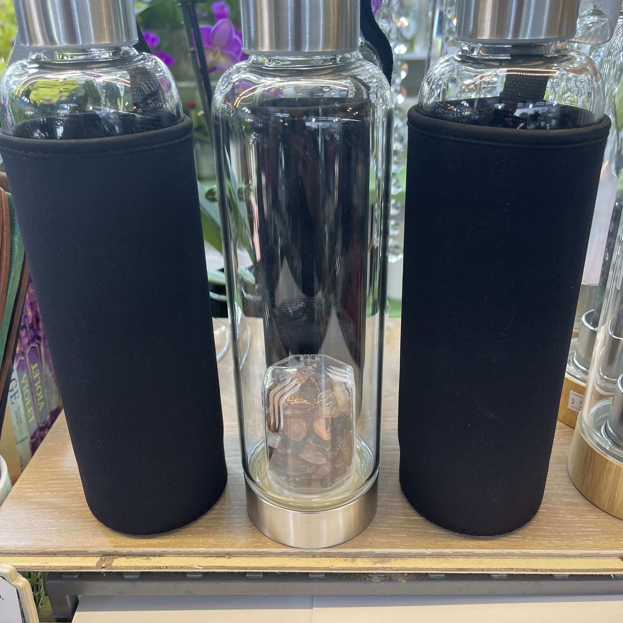 Three clear glass water bottles with black sleeves and silver lids
