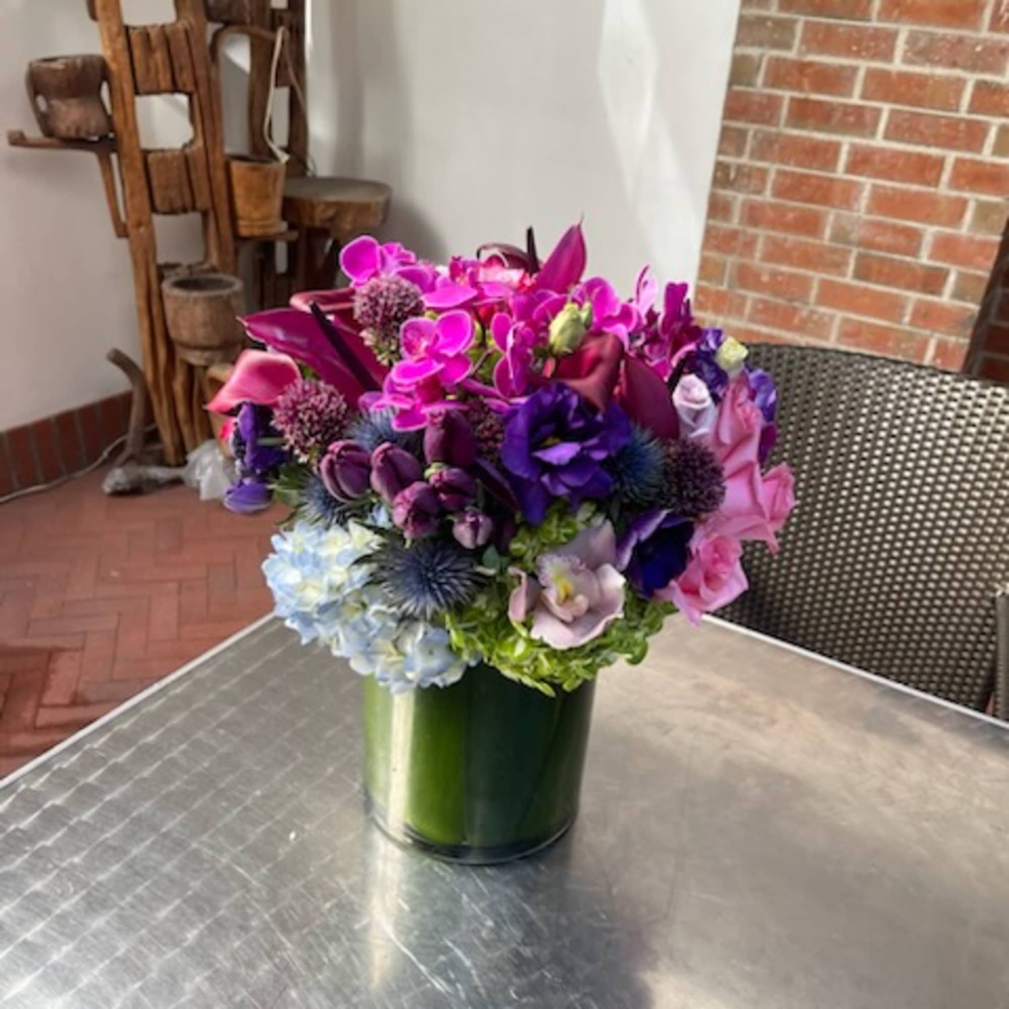 Mixed bouquet of pink, purple, and blue flowers in a green glass vase