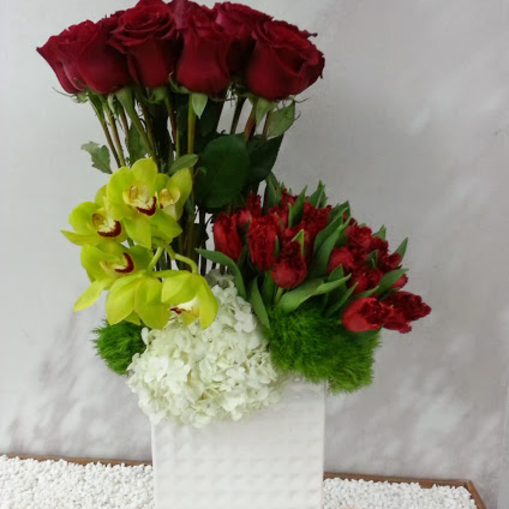 Tall floral arrangement with red roses, yellow orchids, and white hydrangeas in a white vase