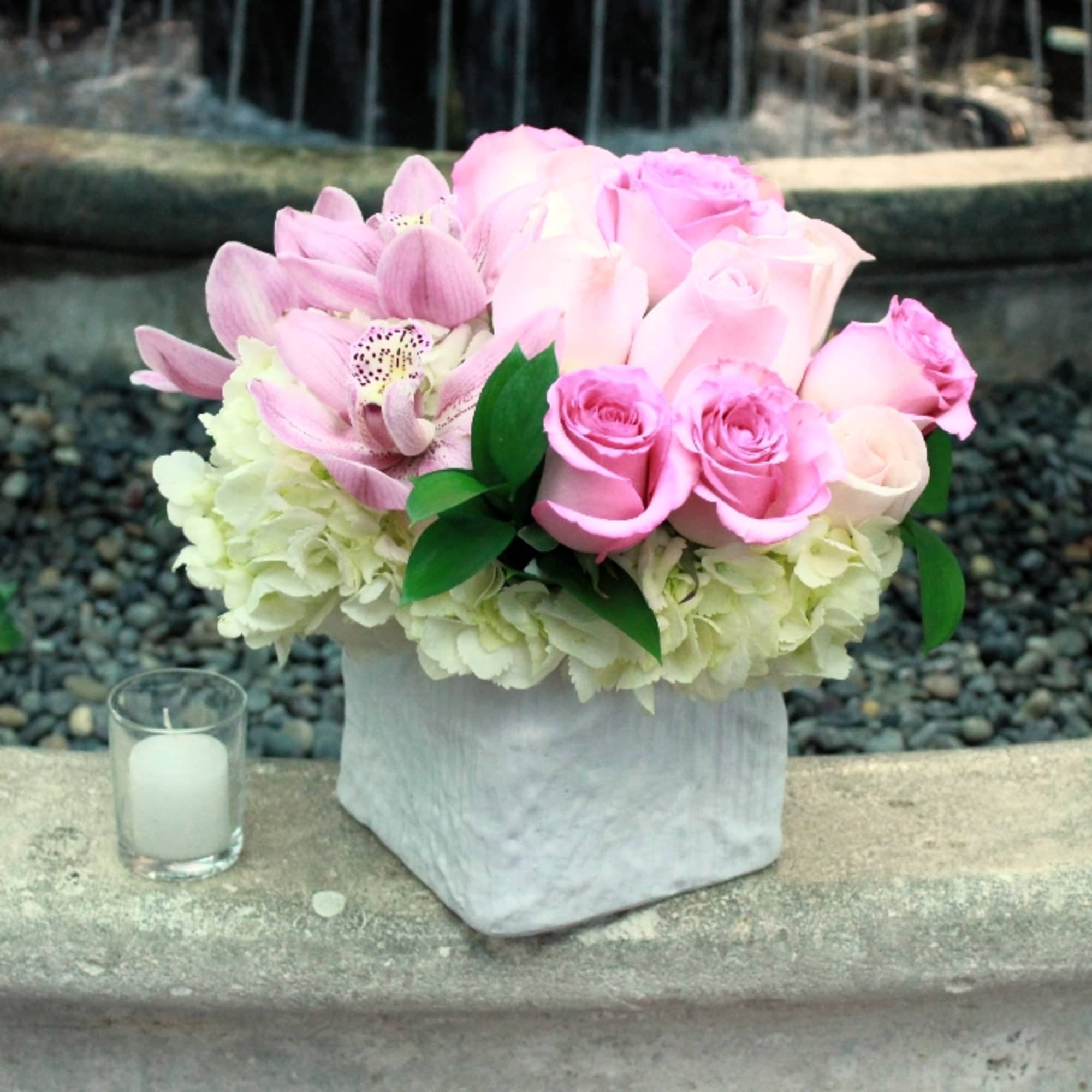 Pink roses and orchids arranged in a white square vase