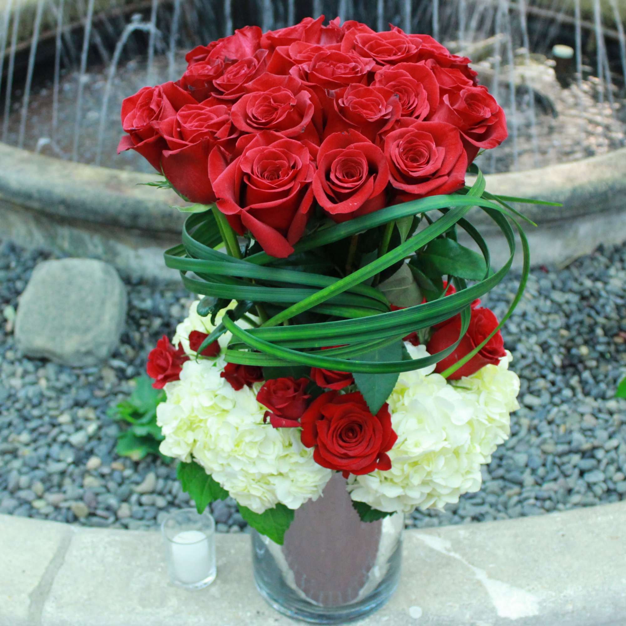 Red roses arranged above white hydrangeas in a glass vase