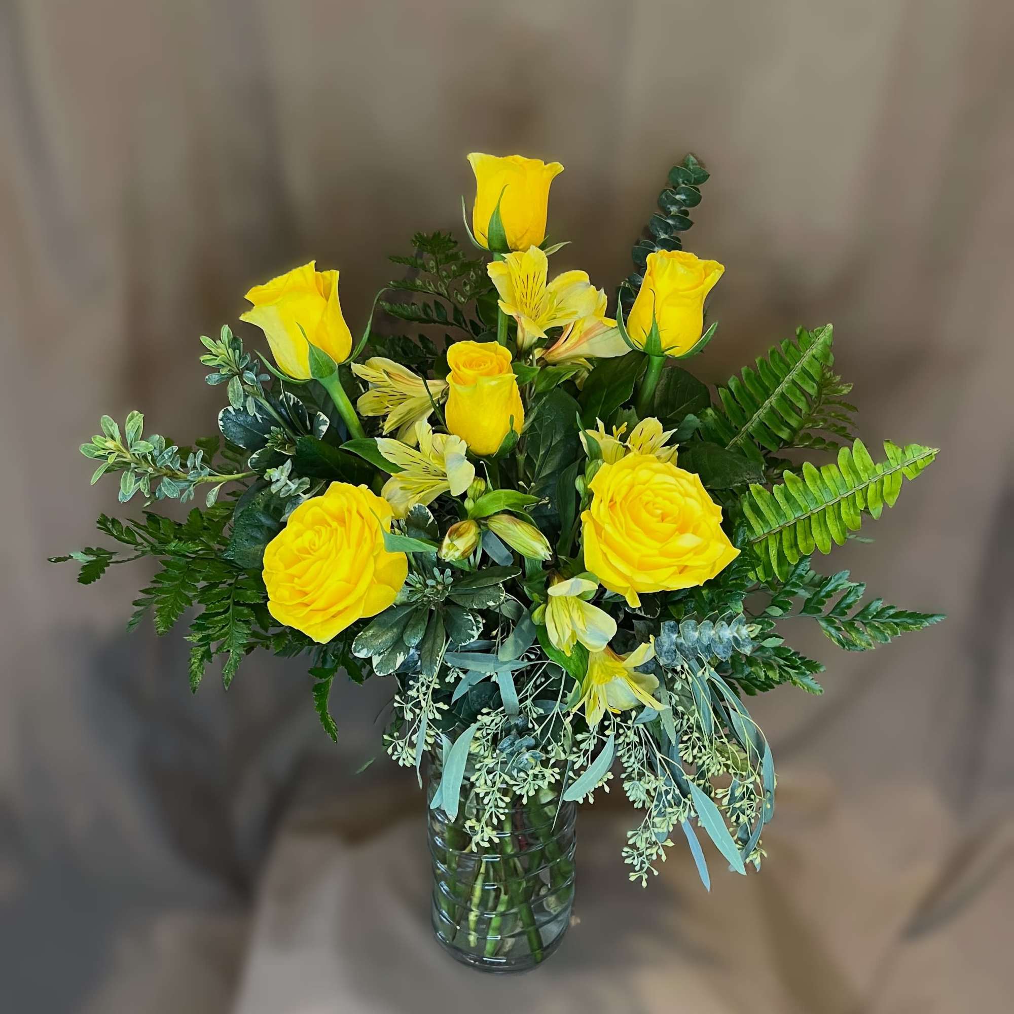 Yellow roses and alstroemeria in a glass vase with mixed greenery