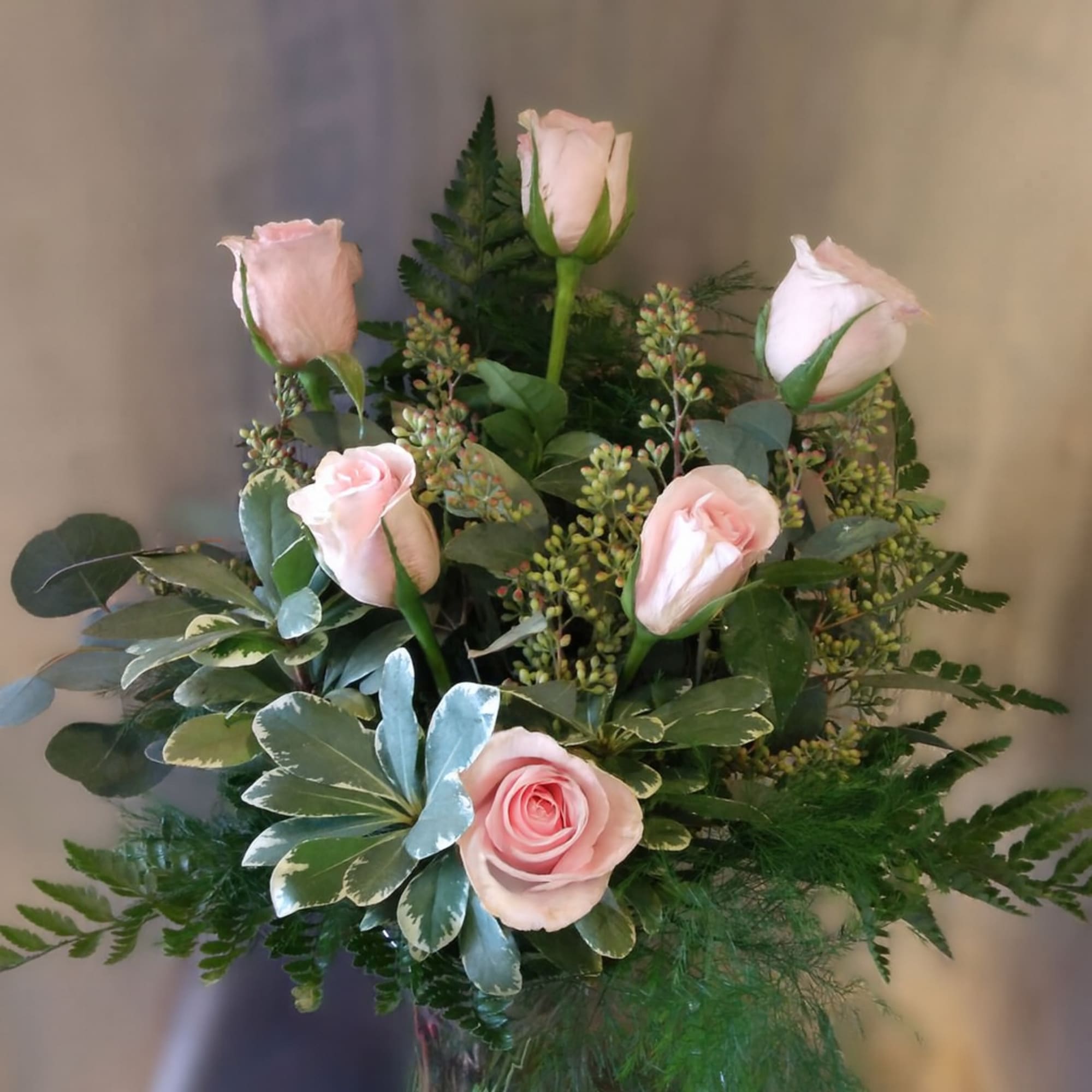 Pink roses arranged in a glass vase with mixed greenery.