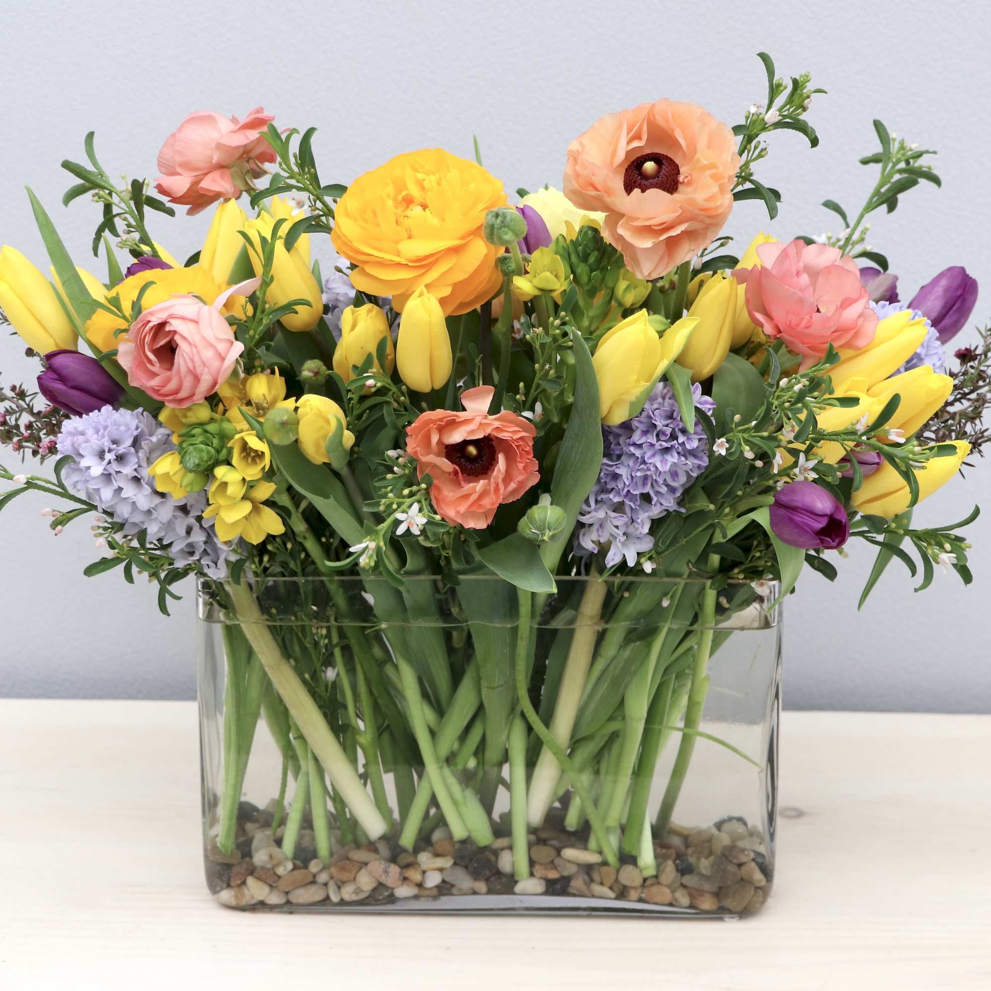 Colorful spring flower arrangement in a rectangular glass vase with river rocks