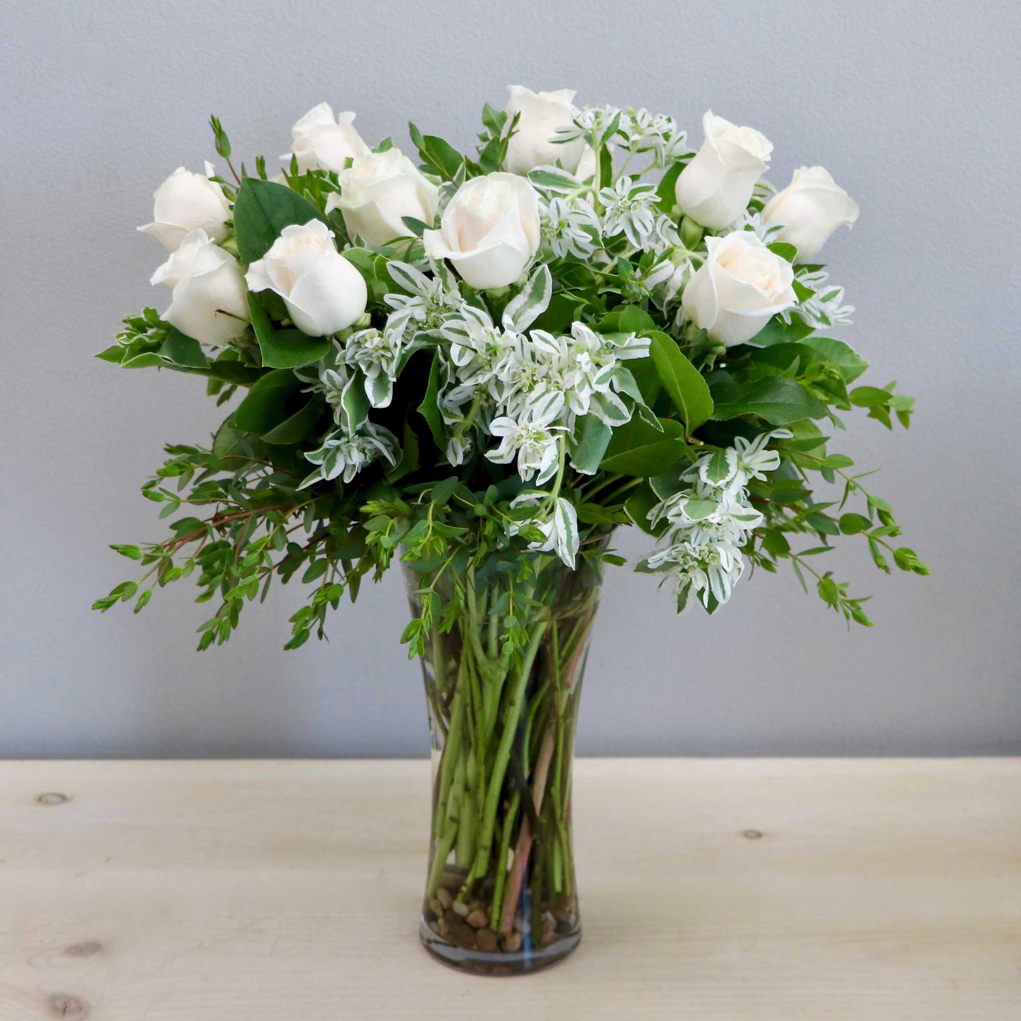 Bouquet of white roses with white variegated accents arranged in a clear glass vase.