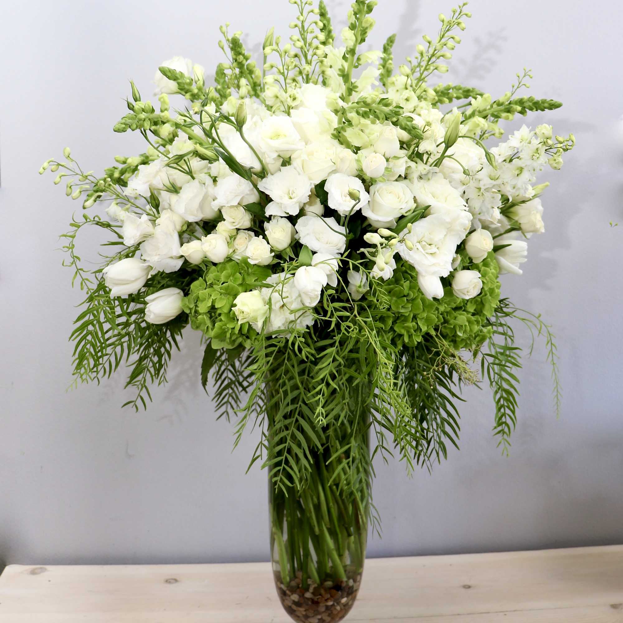 Tall arrangement of white flowers with cascading ferns in a clear glass vase