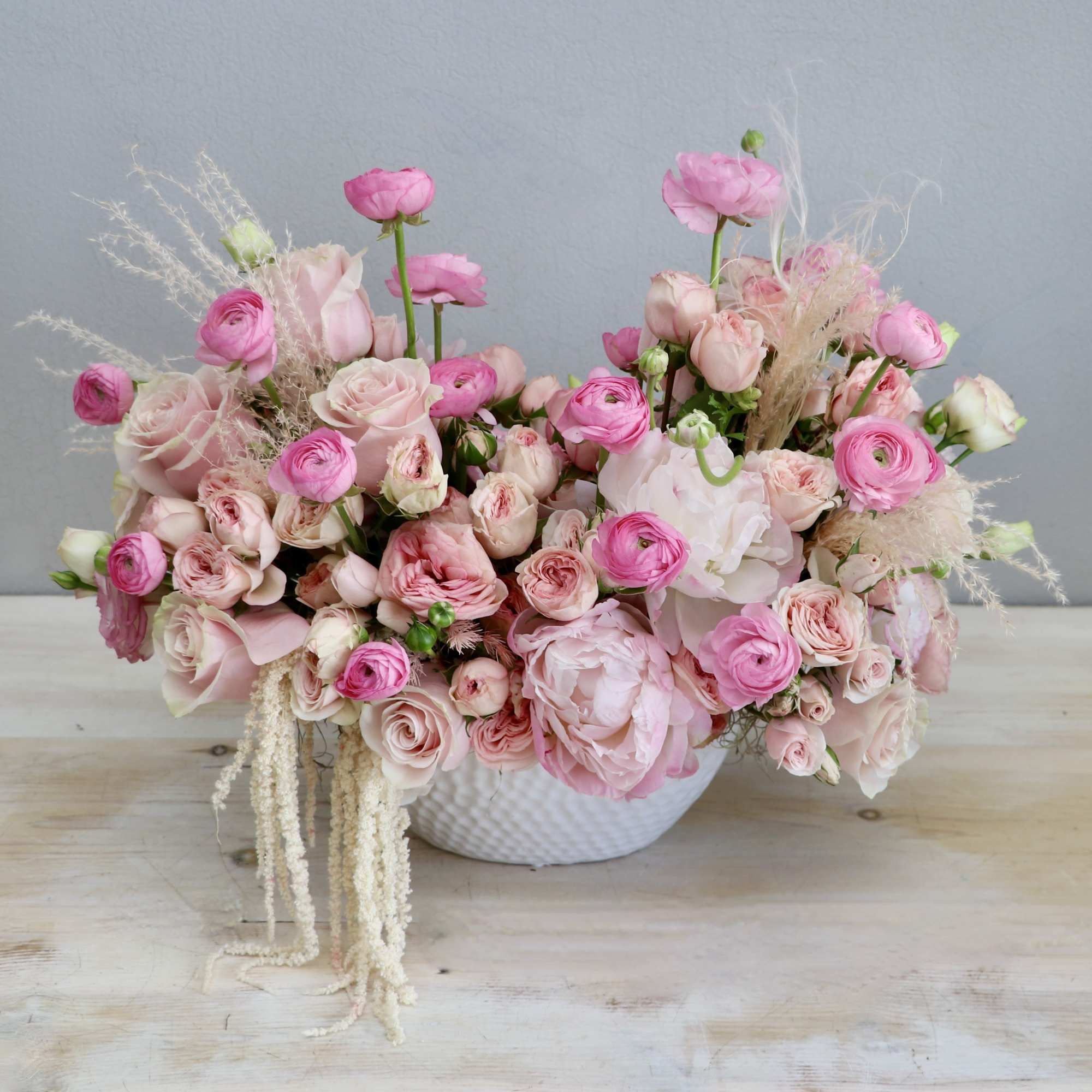 Low bowl arrangement of pink roses, ranunculus, and peonies in a white ceramic container