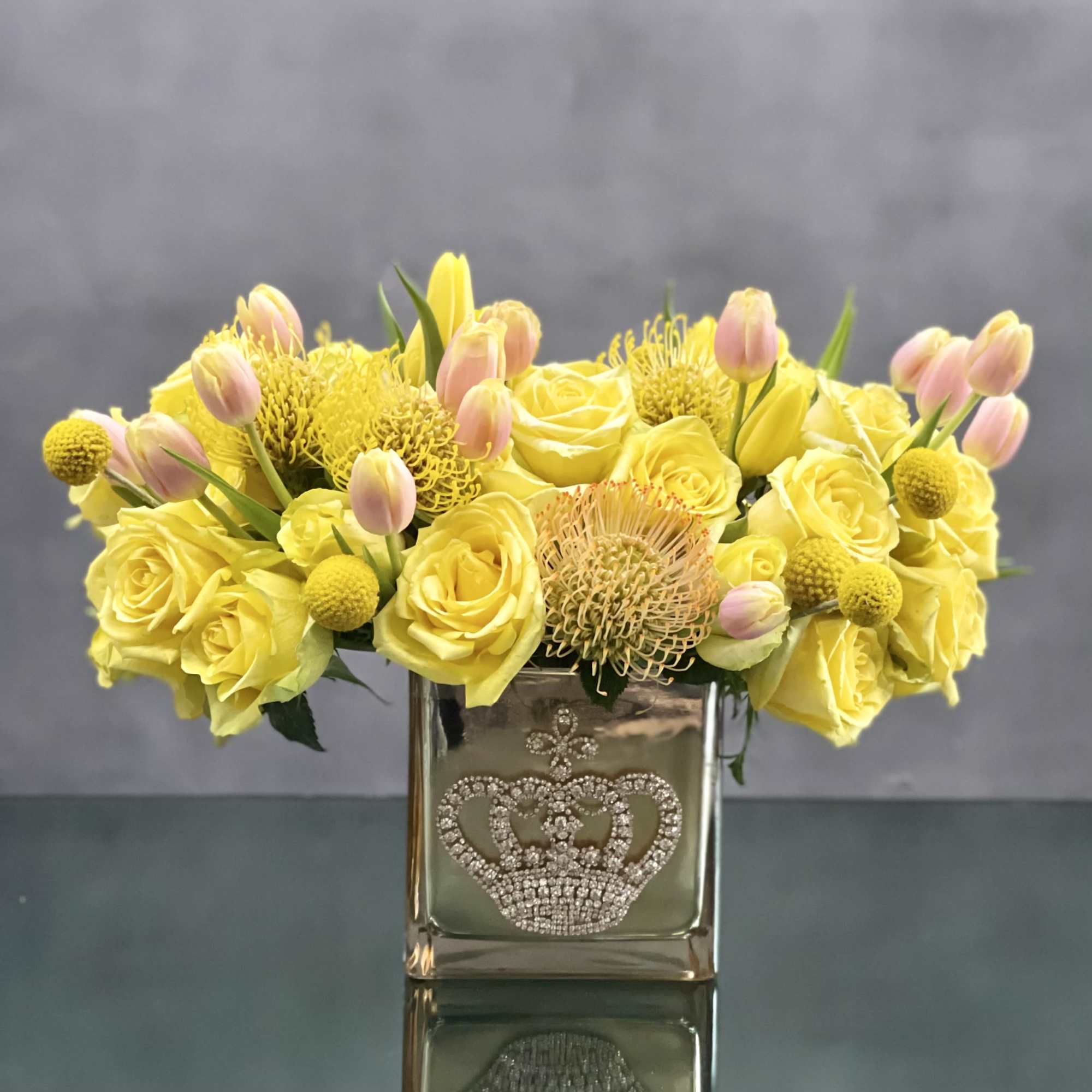 This striking arrangement of yellow roses, tulips and protea in a gold