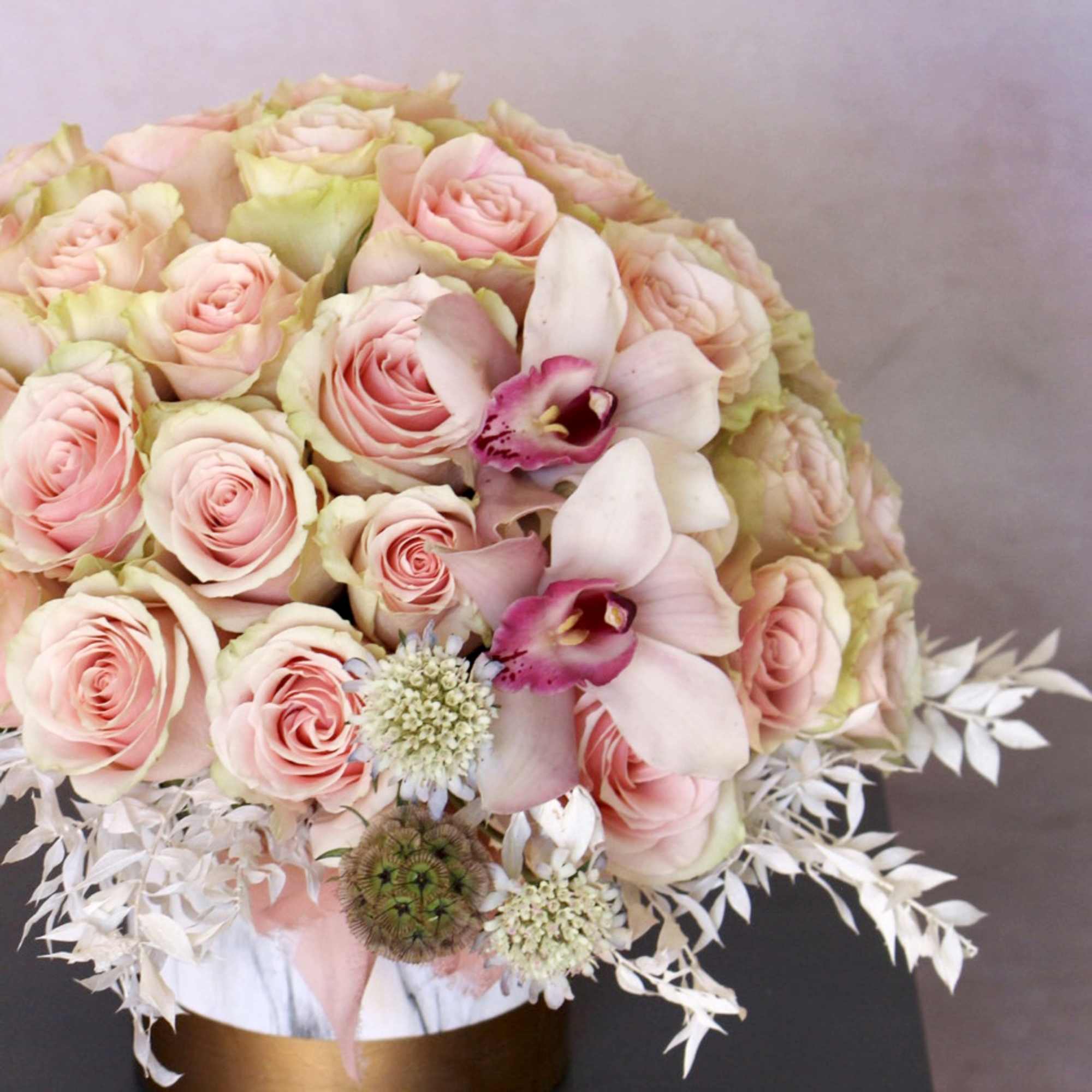 Pink roses and orchids arranged in a round bouquet with white foliage